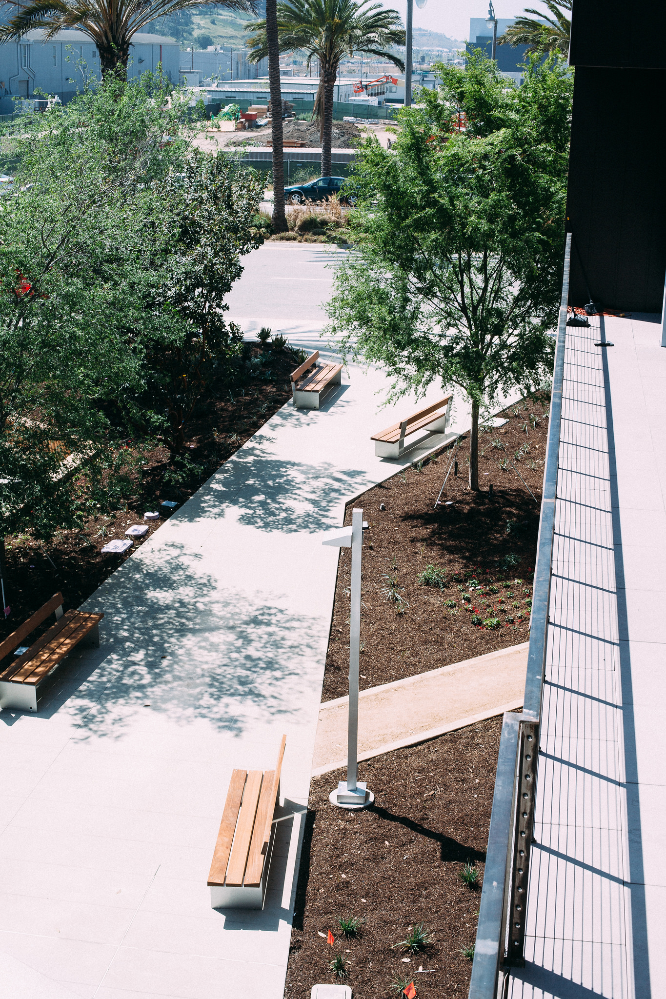 Landscaped courtyard patio with wooden benches, garden mulch, and trees viewed from an upper balcony.