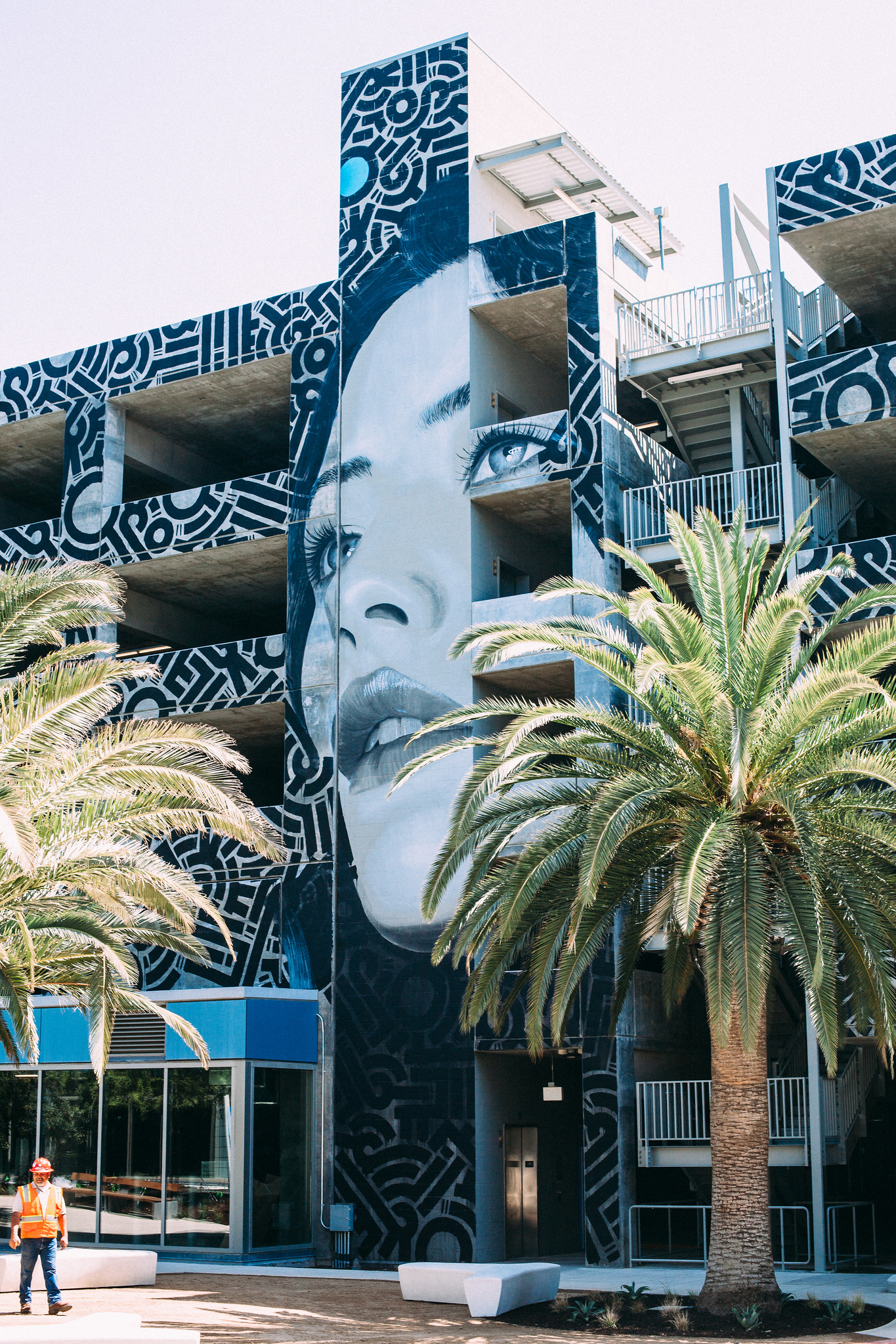 Multi-story parking structure with a large black-and-white mural of a woman's face and palm trees.