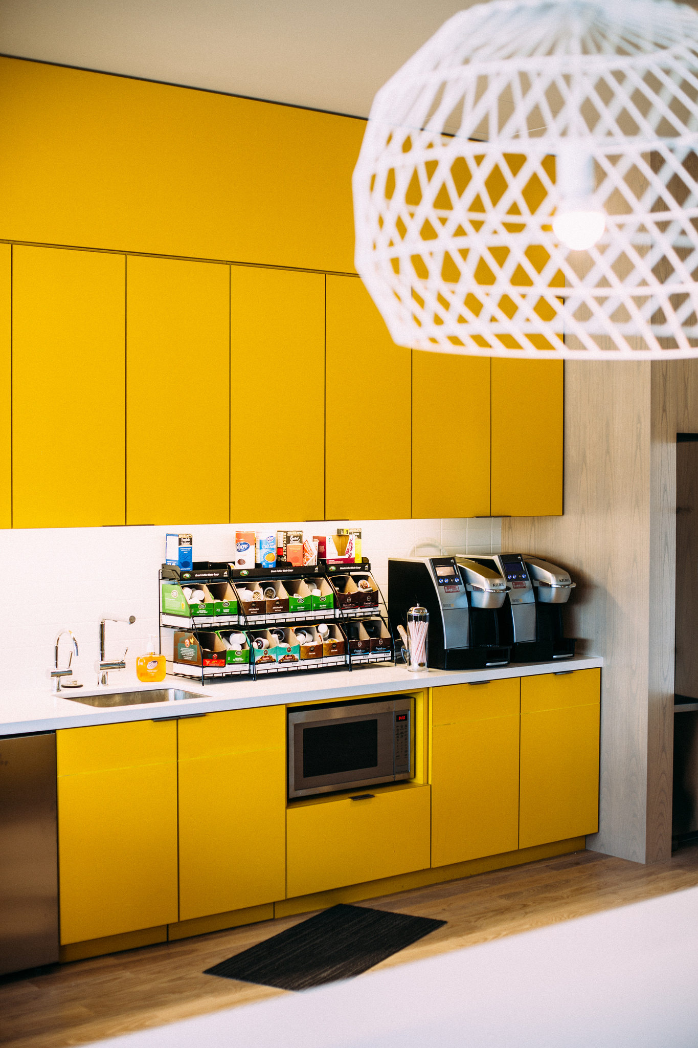 Bright yellow cabinets and countertop in an office kitchenette with coffee makers and a microwave.