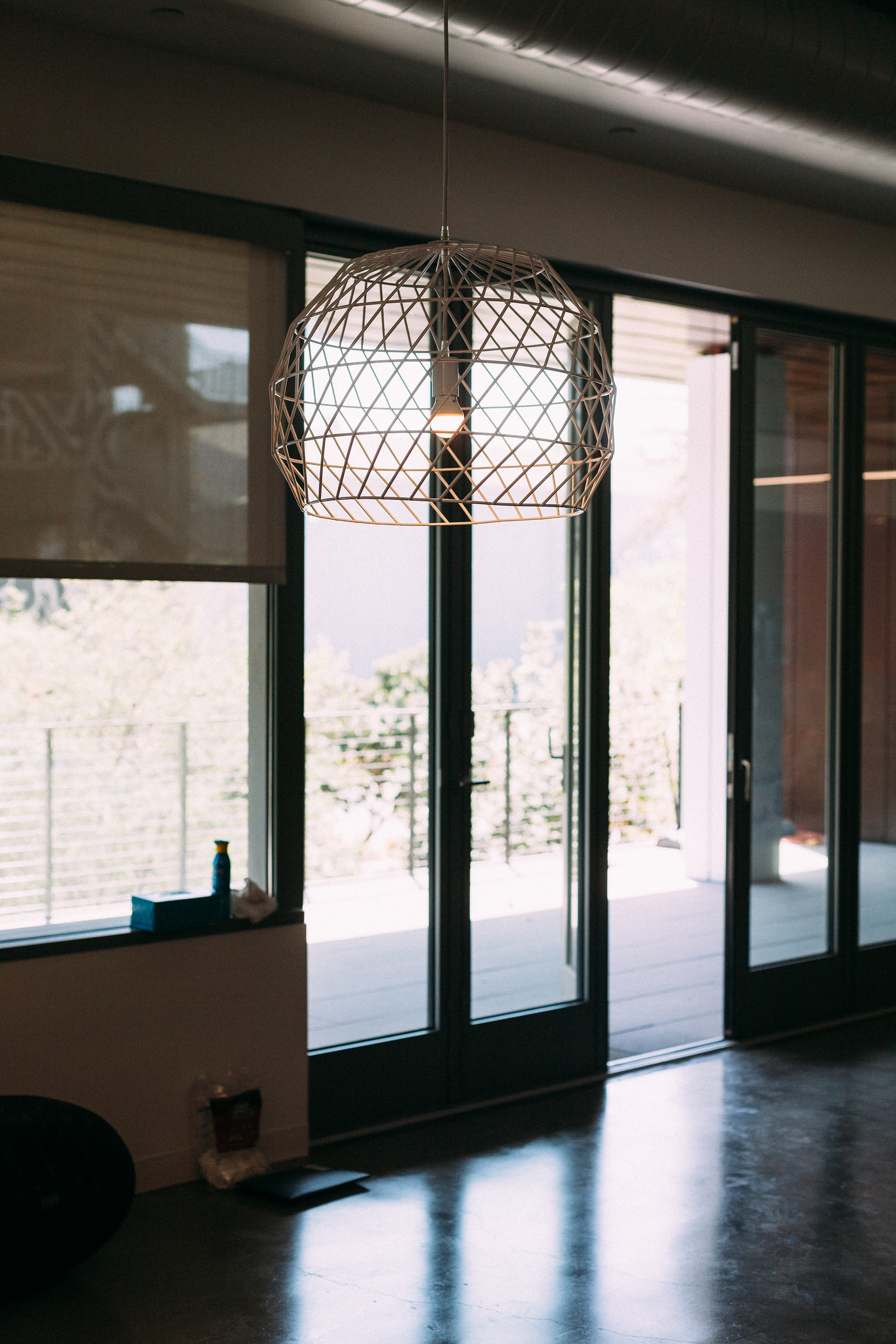 Geometric white wireframe dome pendant light illuminated above dark concrete floors in front of glass patio doors.