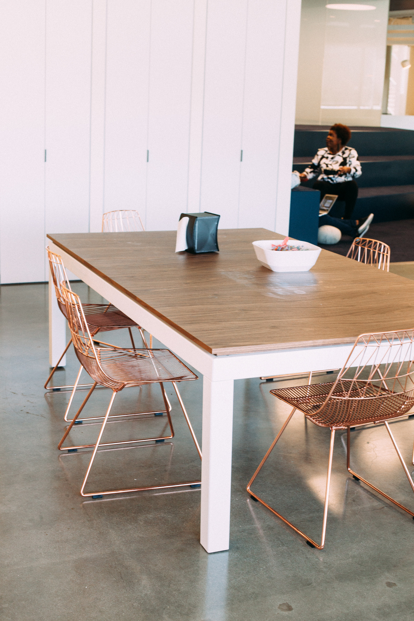 Light wood dining table with copper wire chairs on polished concrete floors in a modern office cafeteria.