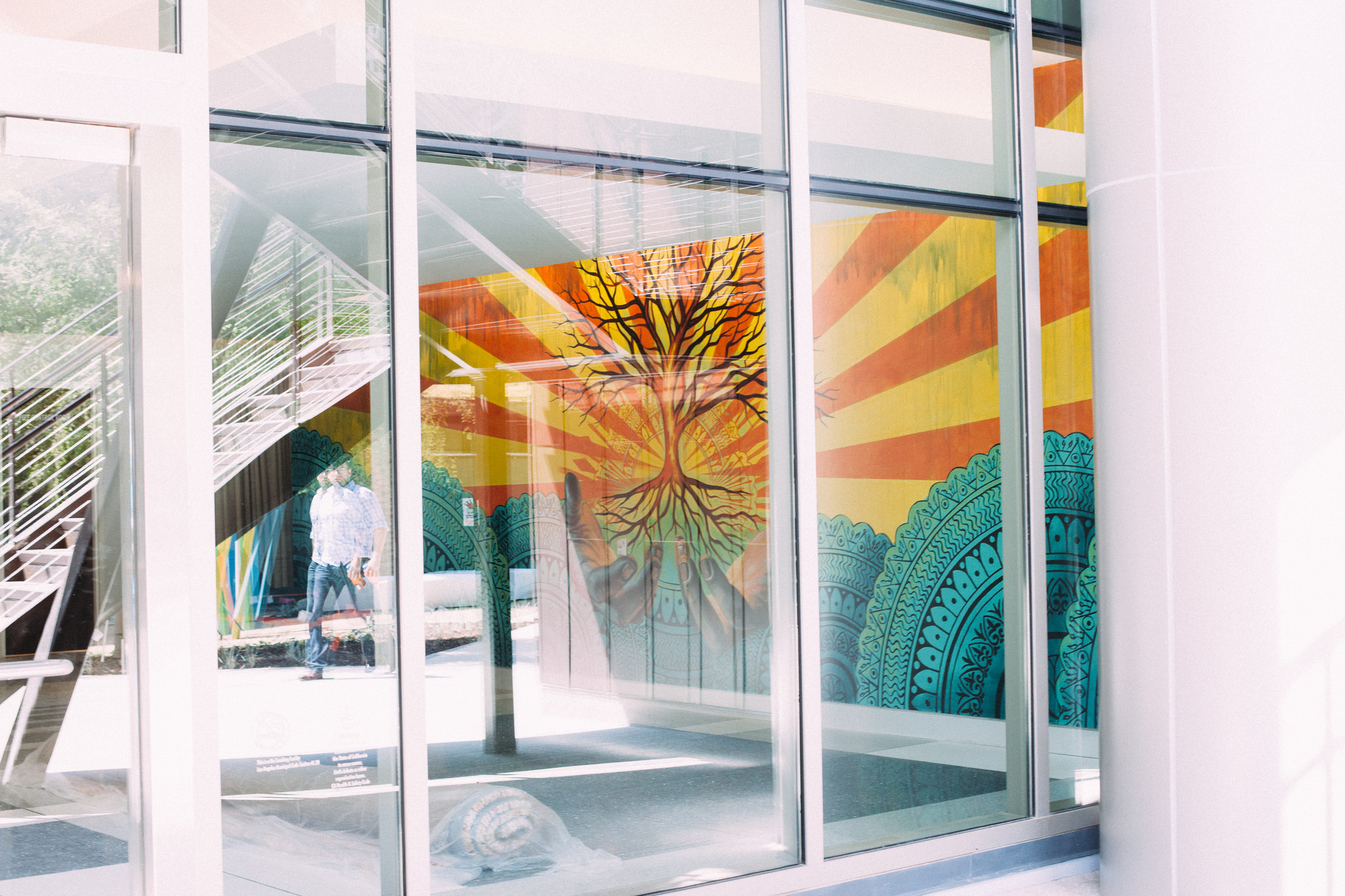 Glass entryway reflecting stairs and displaying an interior mural of a tree with radiant sunburst rays.