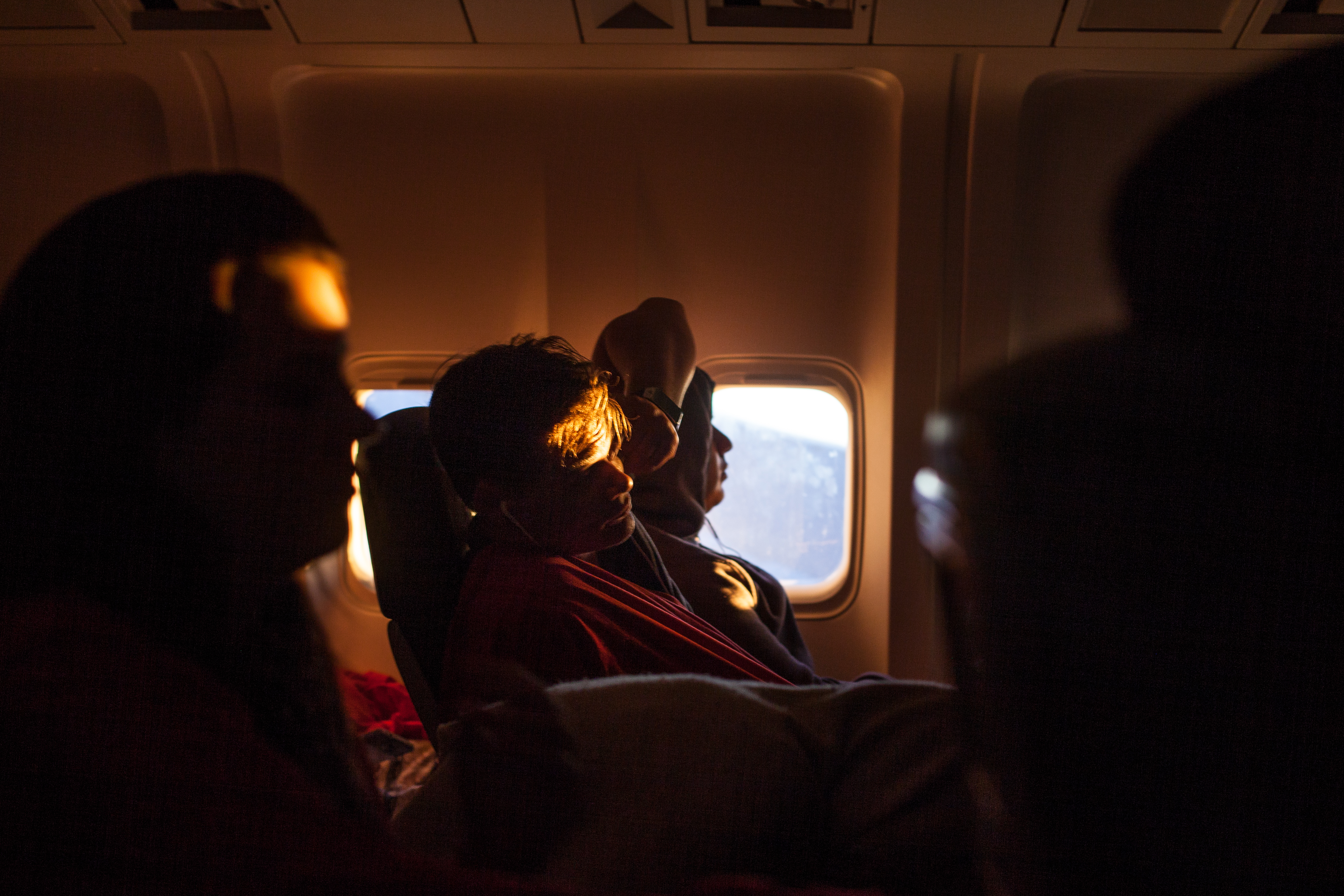 Passenger resting his head in a darkened airplane cabin with golden sunlight catching his forehead, shot with a Canon 5D Mark II.
