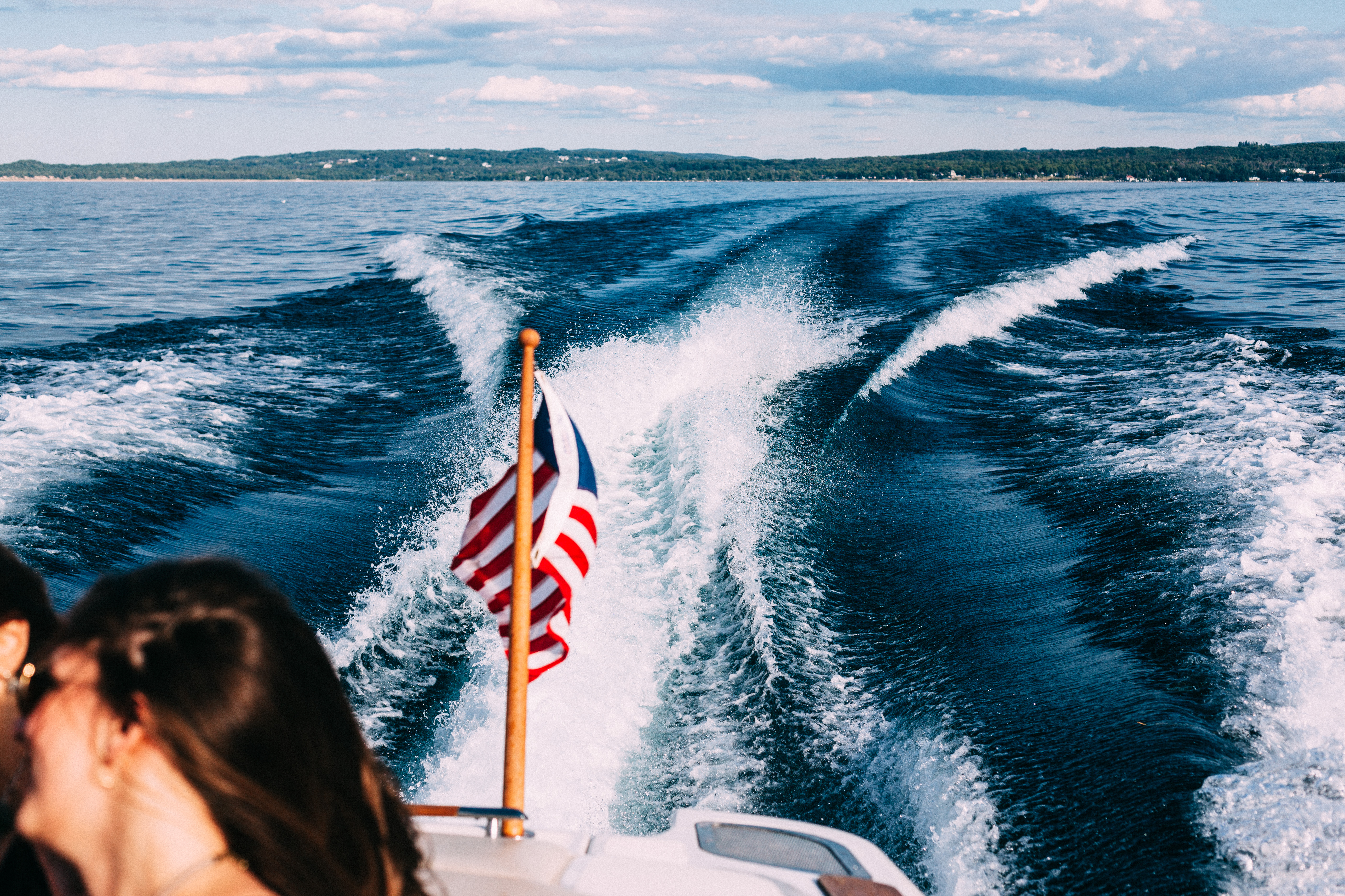 Foamy white and blue wake streaming behind a speeding motorboat flying a small American flag from its stern, shot with a Canon 5D Mark II.