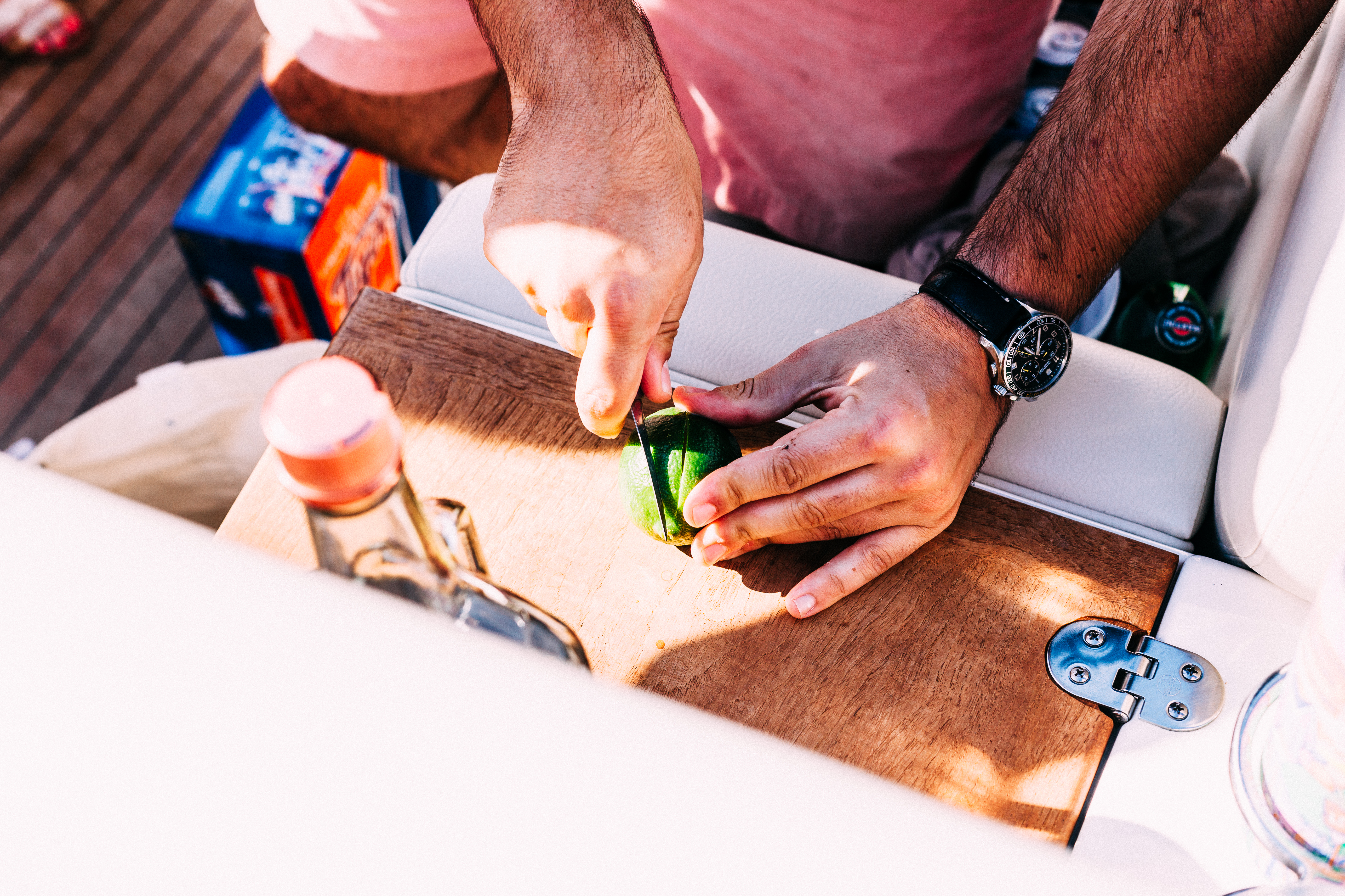 Close-up of hands using a paring knife to slice a fresh green lime on a wooden cutting board aboard a boat, shot with a Canon 5D Mark II.