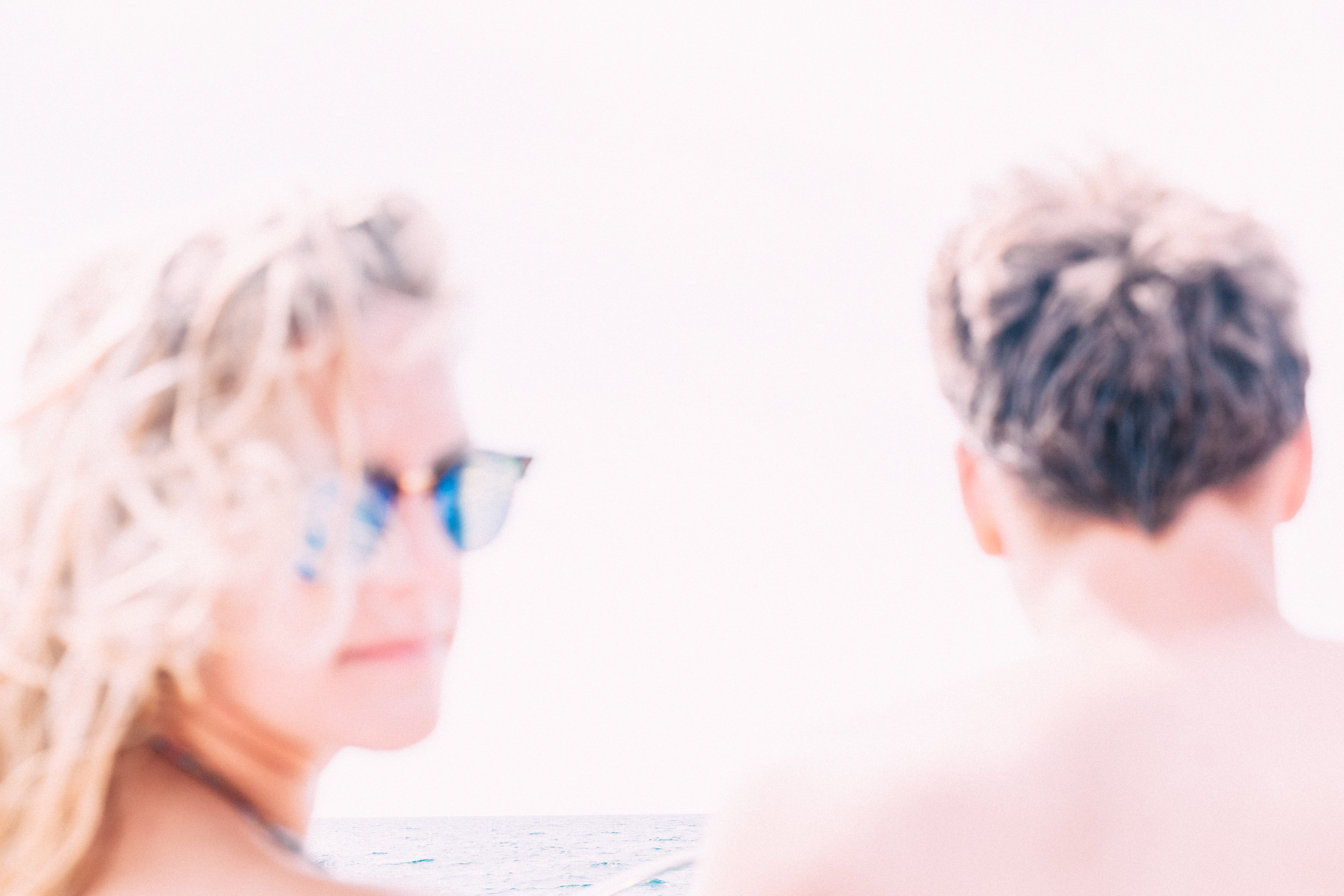 Blonde woman in sunglasses and a young man seated on a boat under bright sunlit overexposed daylight.