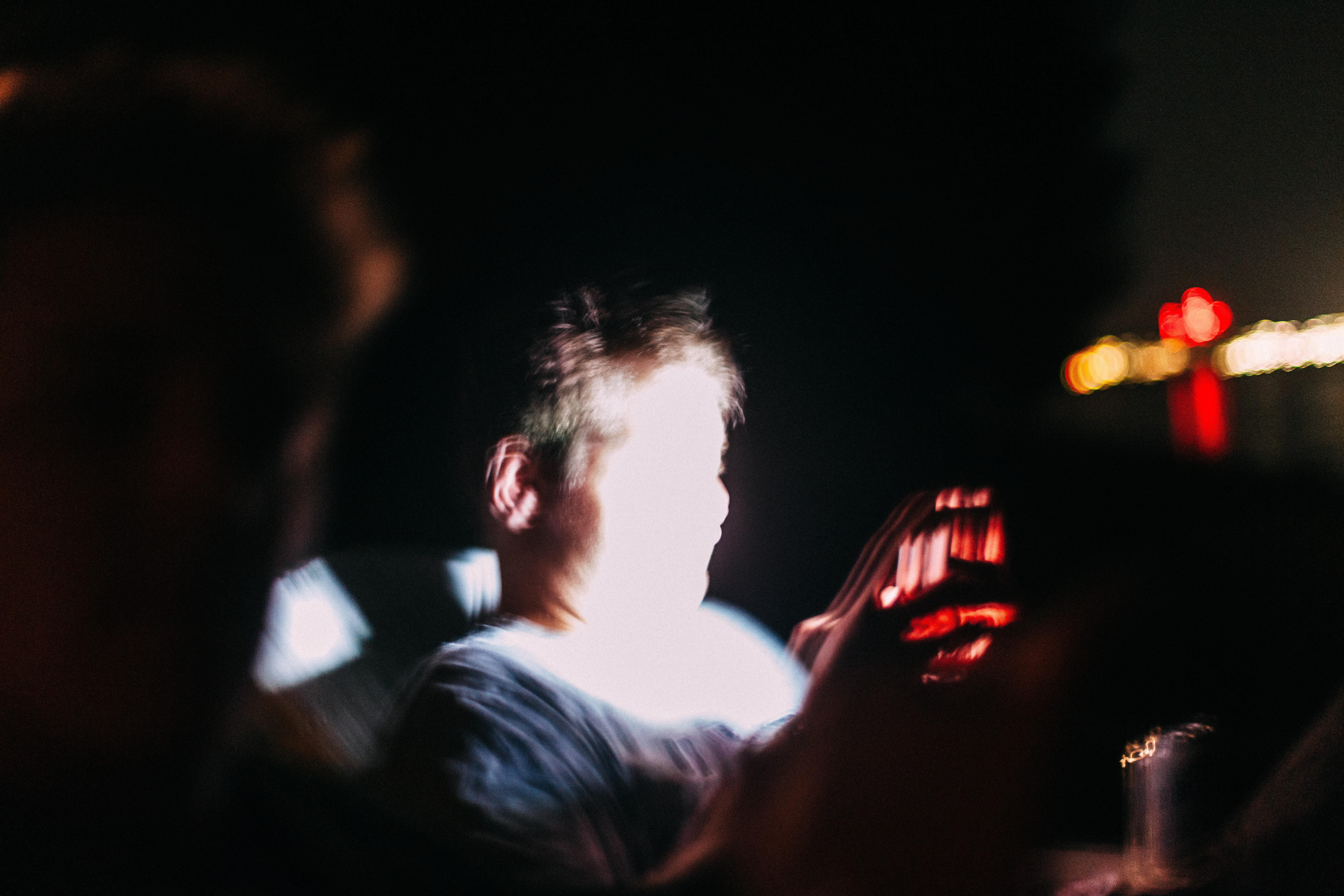 Intimate candid of a person in the dark holding a glowing smartphone screen illuminating their face at night.