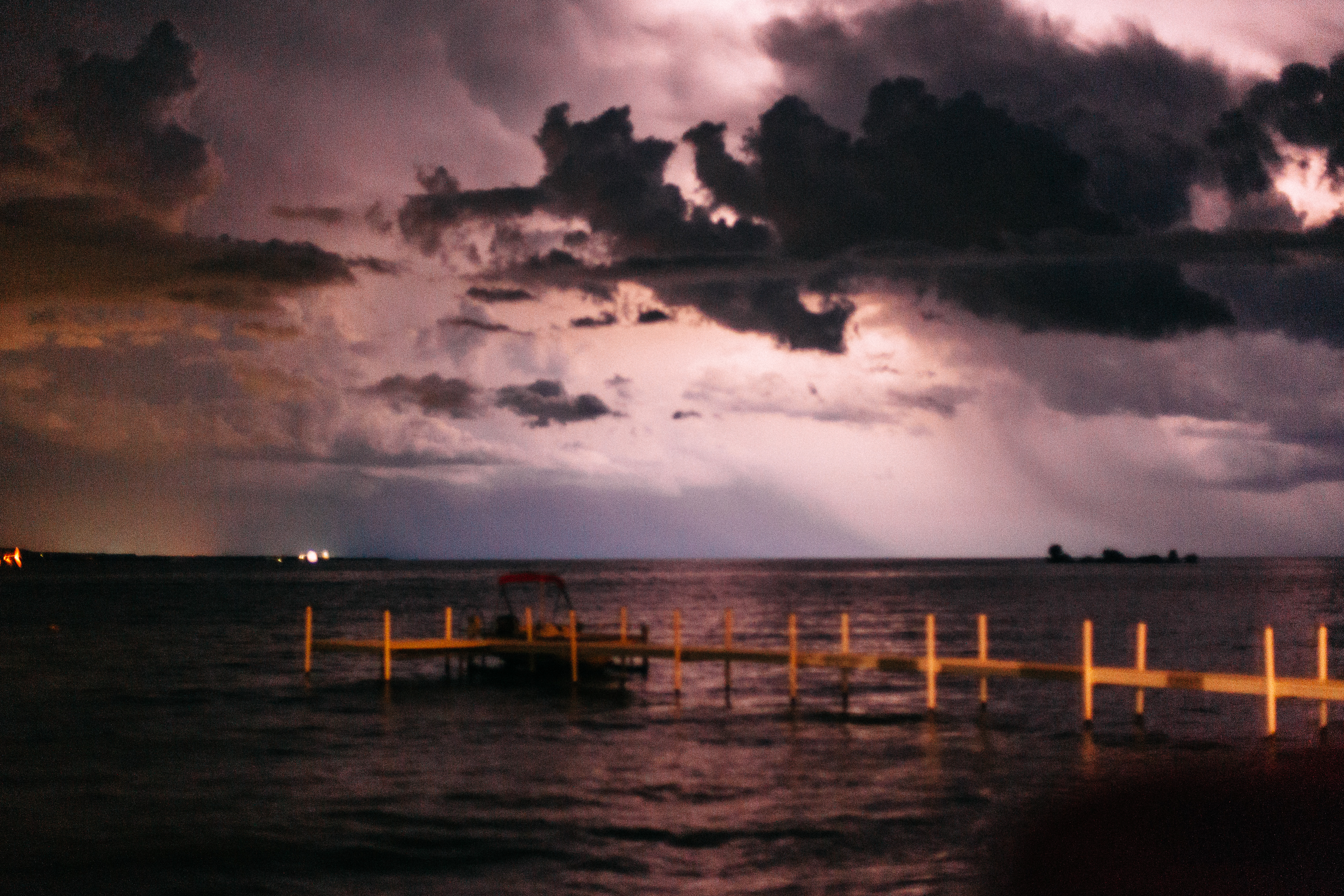 Dramatic storm over a lake with lightning illuminating dark clouds above a dock and pontoon boat.