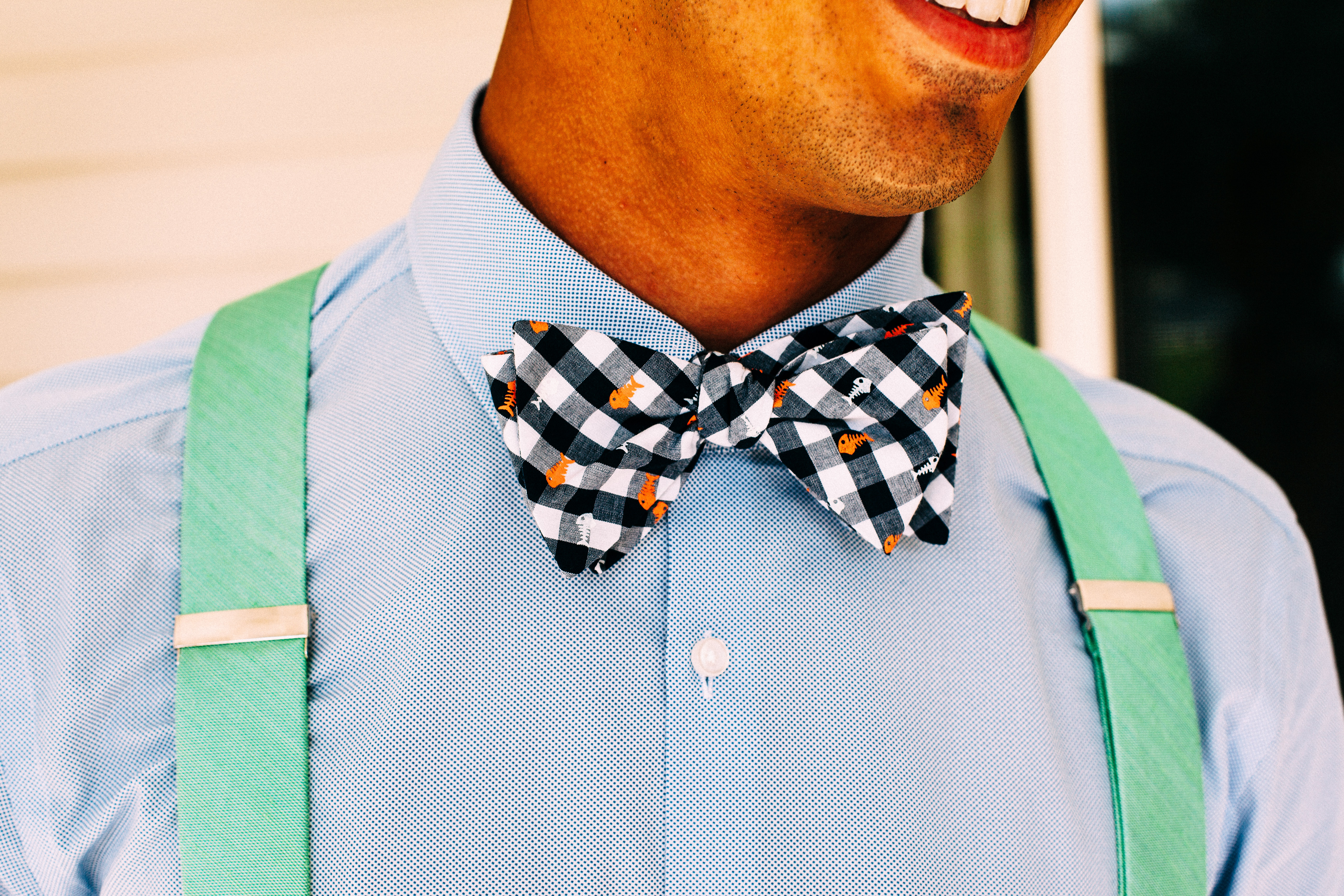 Groomsman in light blue shirt, green suspenders, and gingham bow tie patterned with orange fish skeletons.
