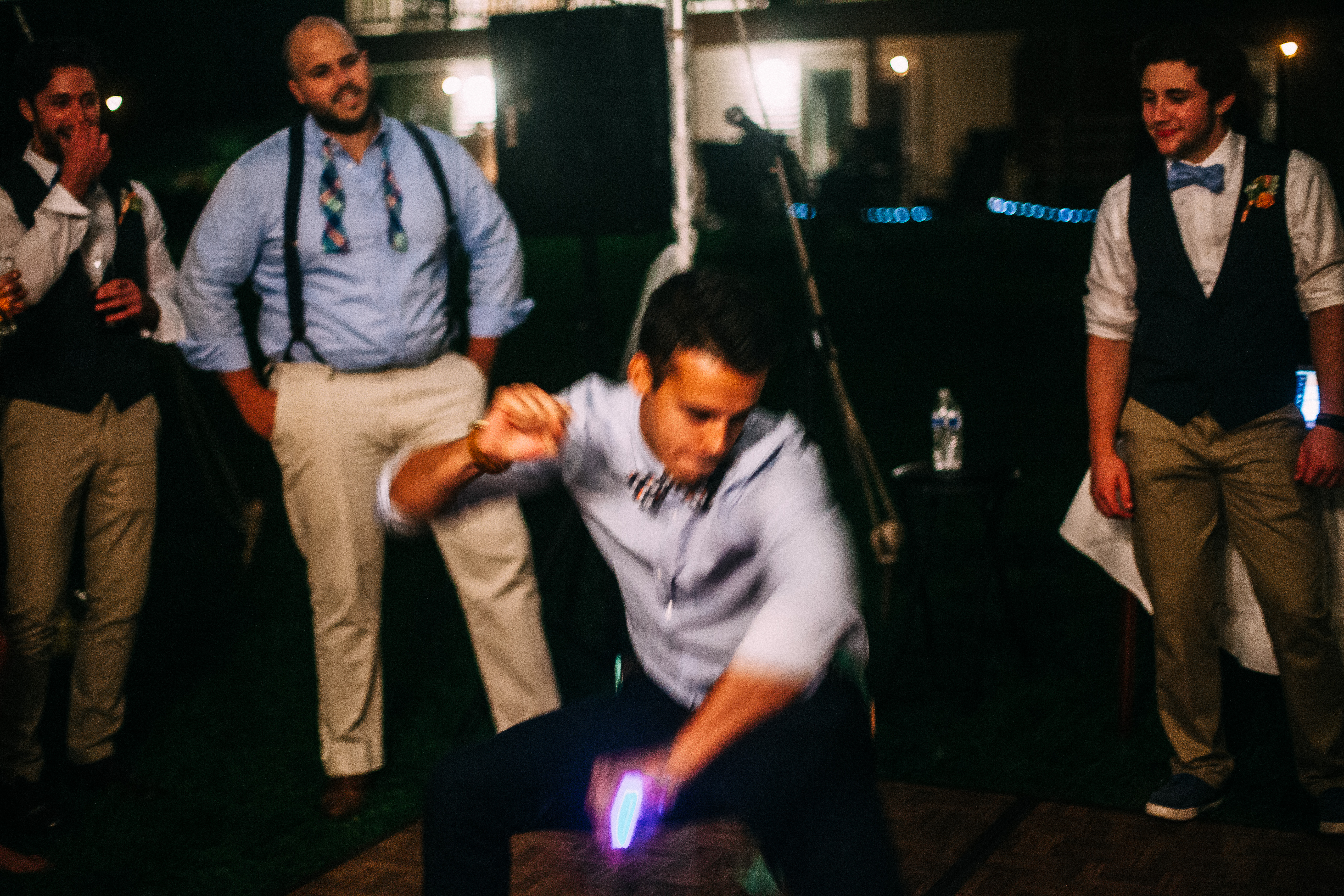Wedding guest breakdancing on the floor with a glowing bracelet as groomsmen watch and laugh.