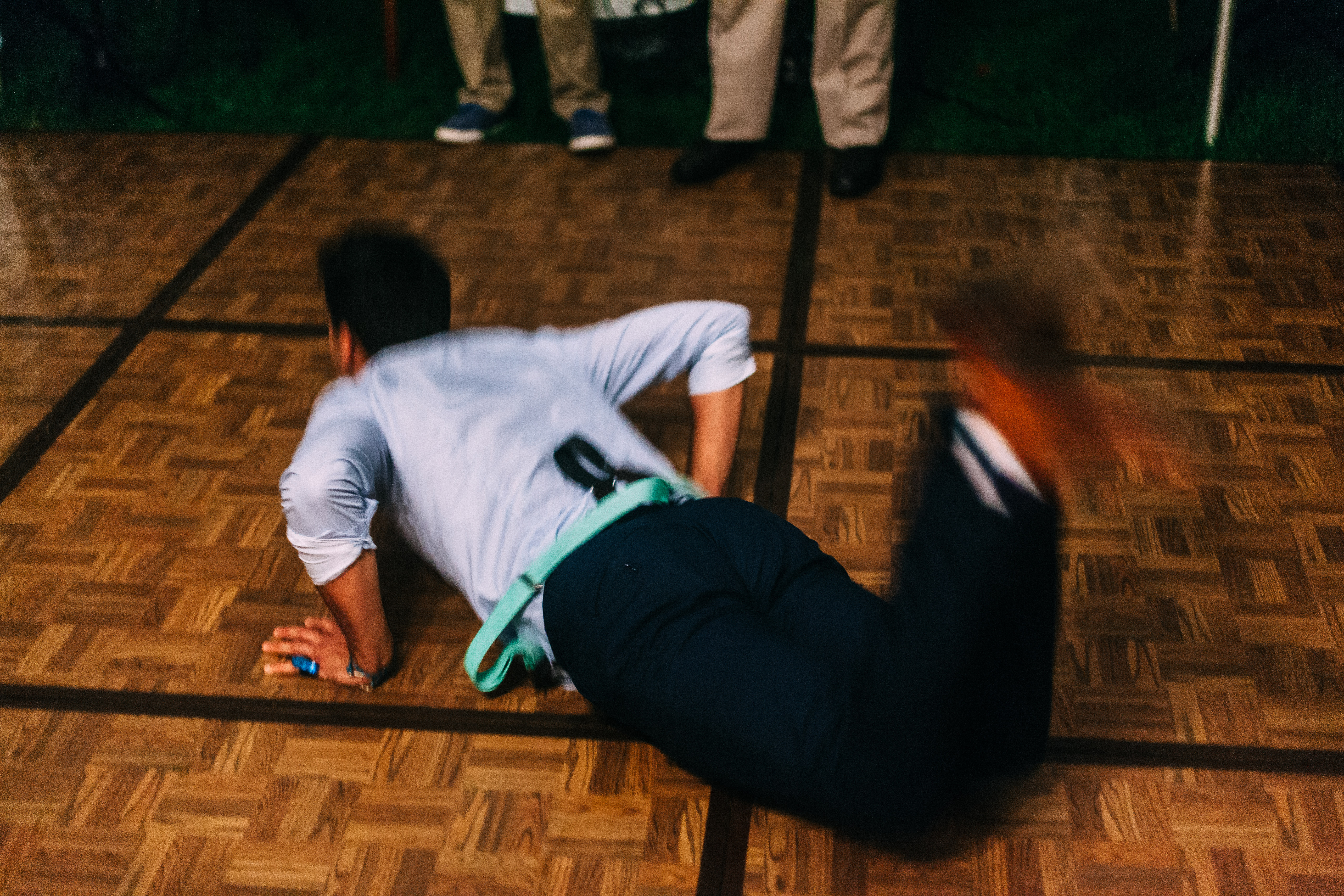 A man doing the worm dance move across the wooden parquet dance floor at a nighttime outdoor wedding reception.