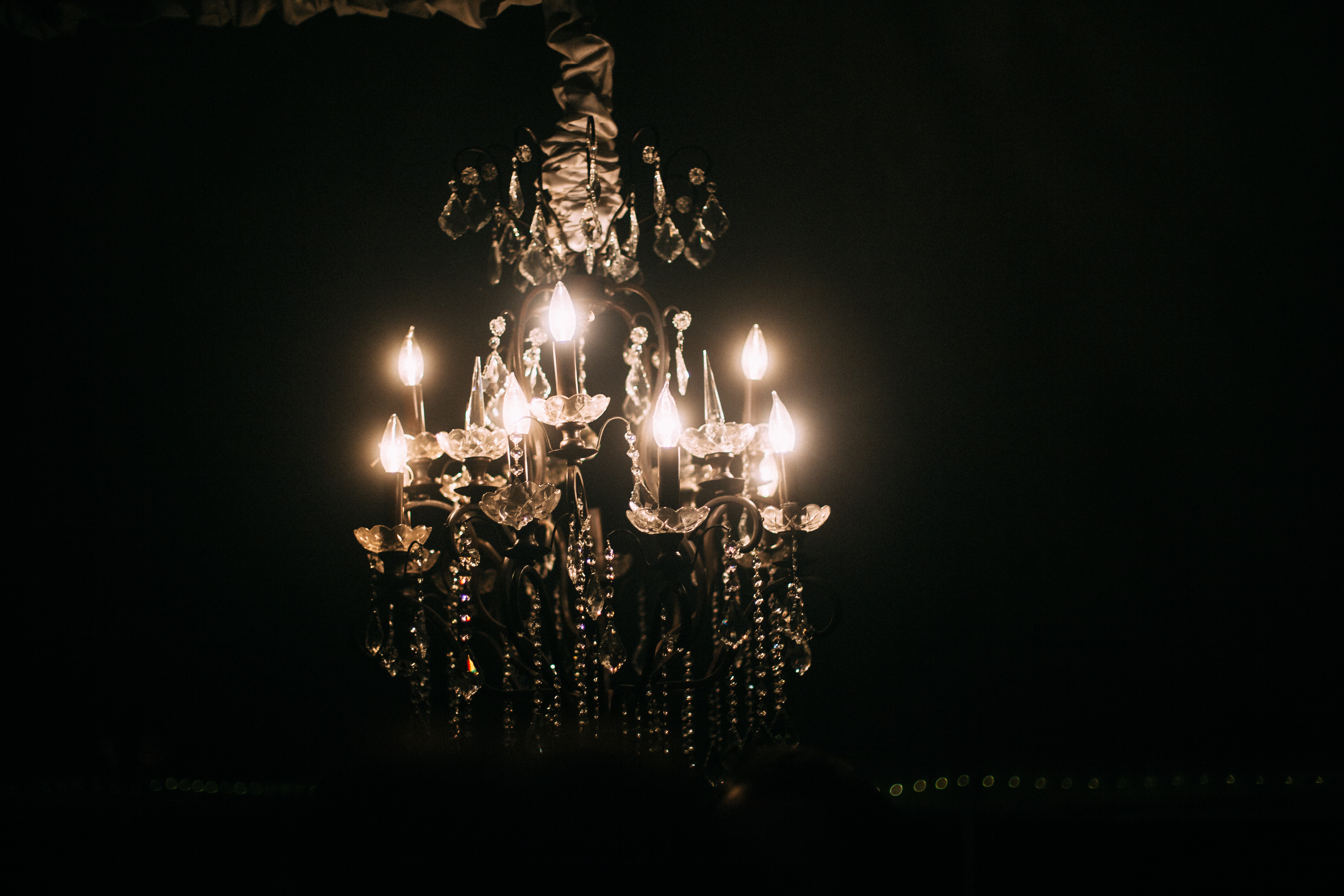 Ornate crystal chandelier with glowing candle bulbs suspended inside a reception tent at night.