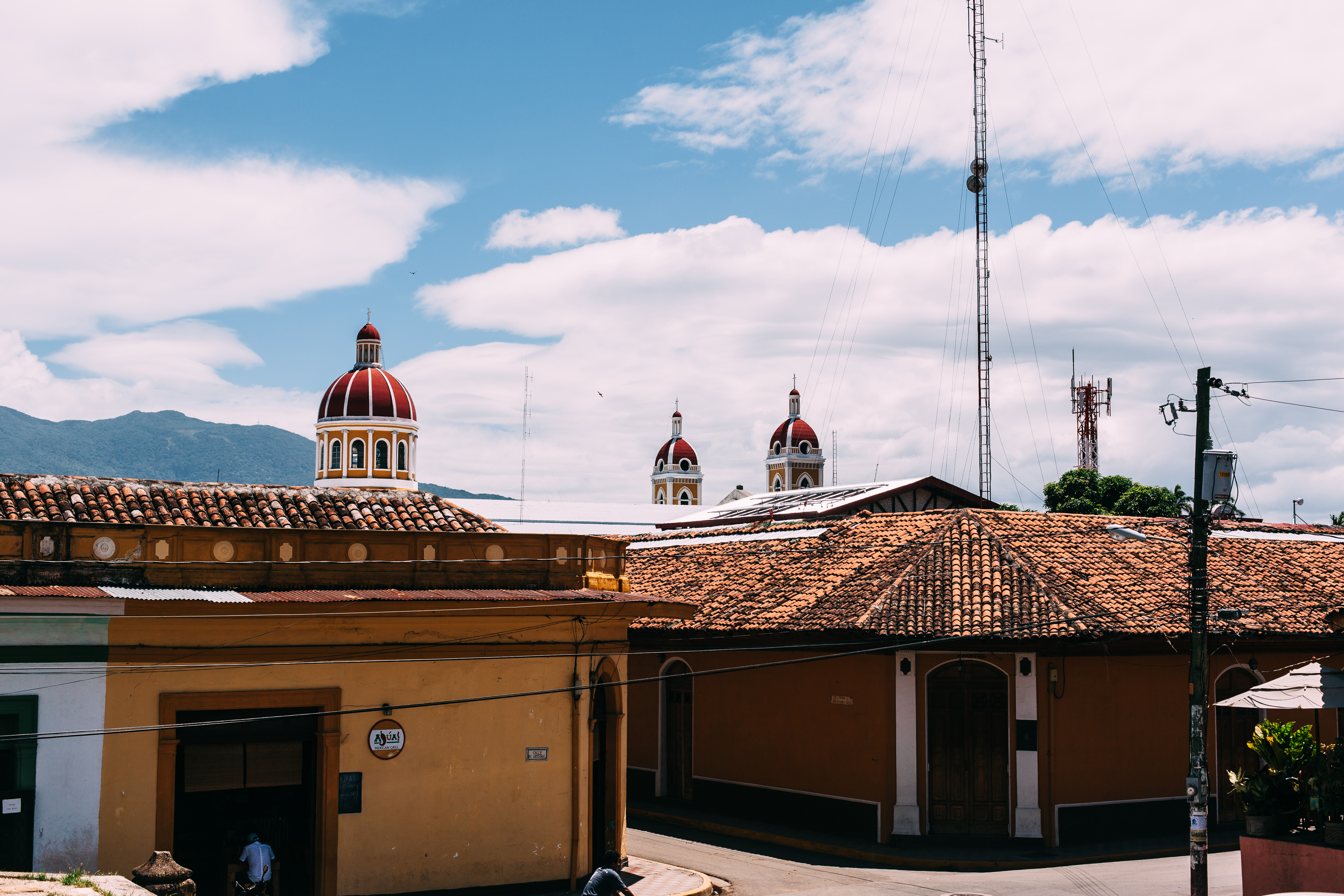 Rooftop view of terracotta houses and yellow Granada Cathedral domes against volcanic hills in Nicaragua.