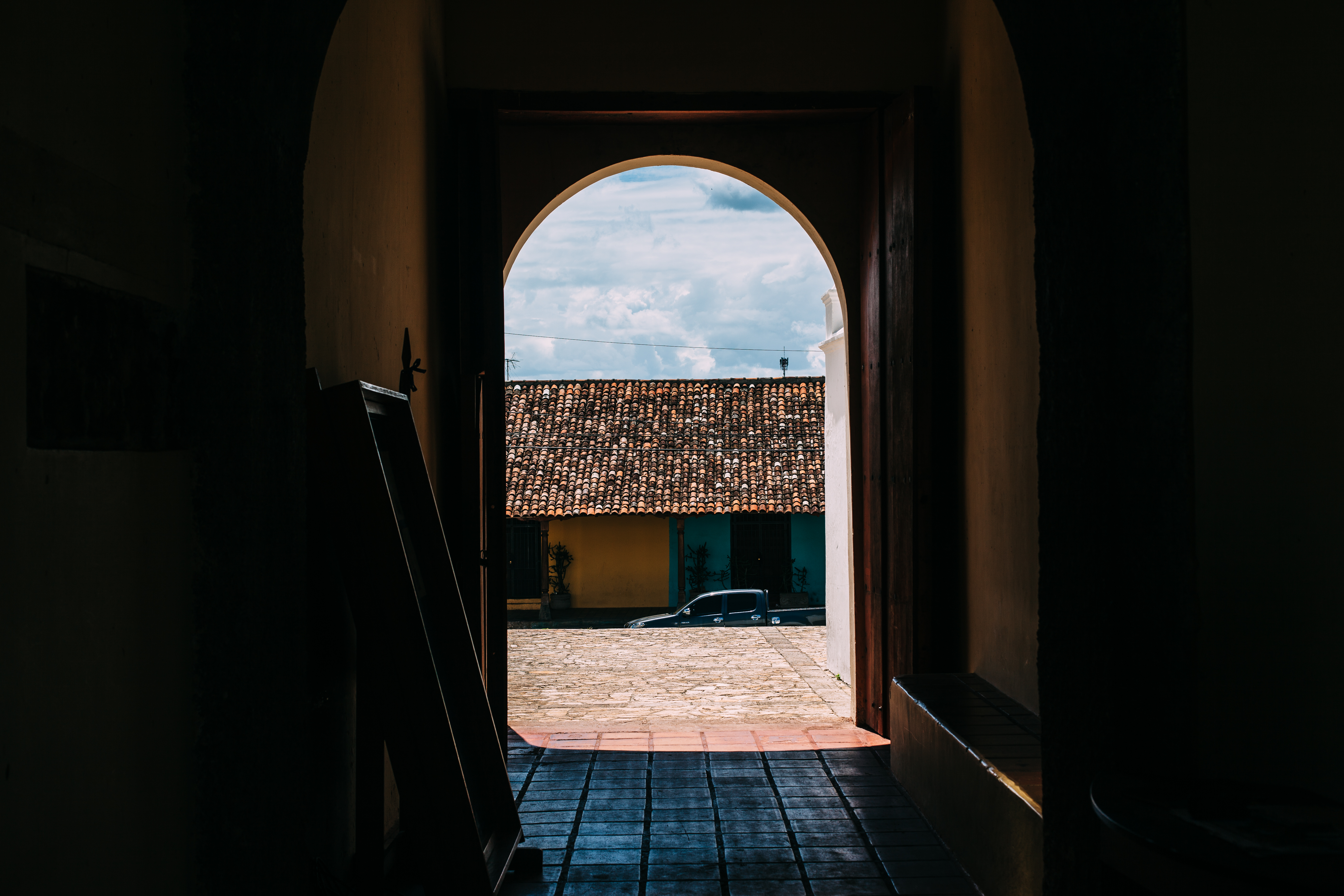 Arched doorway view onto a sunlit cobblestone courtyard and colonial buildings in Granada, Nicaragua.