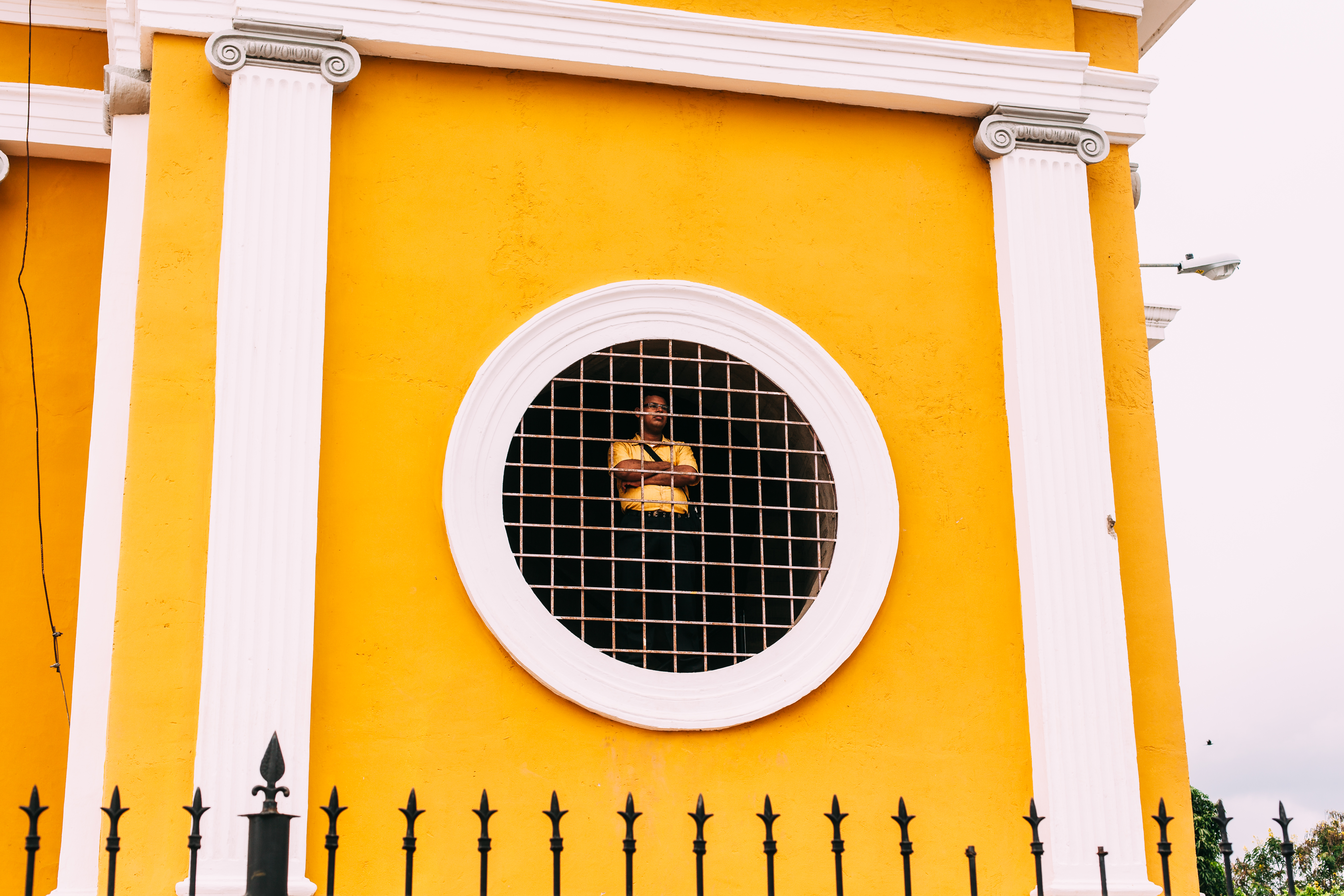 Man looking out through a round grated window in the yellow wall of Granada Cathedral in Nicaragua.