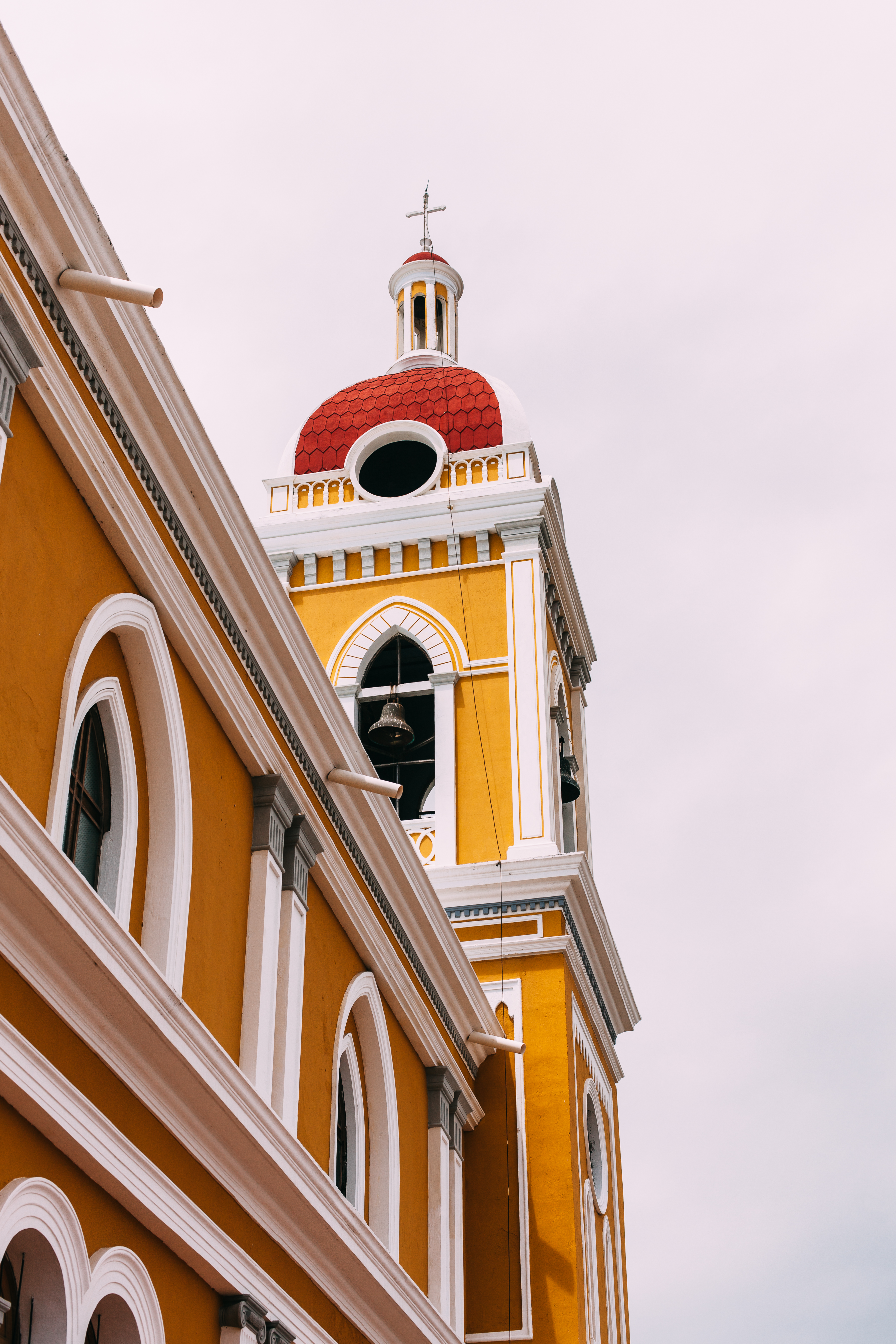 Upward view of the yellow and white facade of Granada Cathedral toward its arched bell tower and dome.