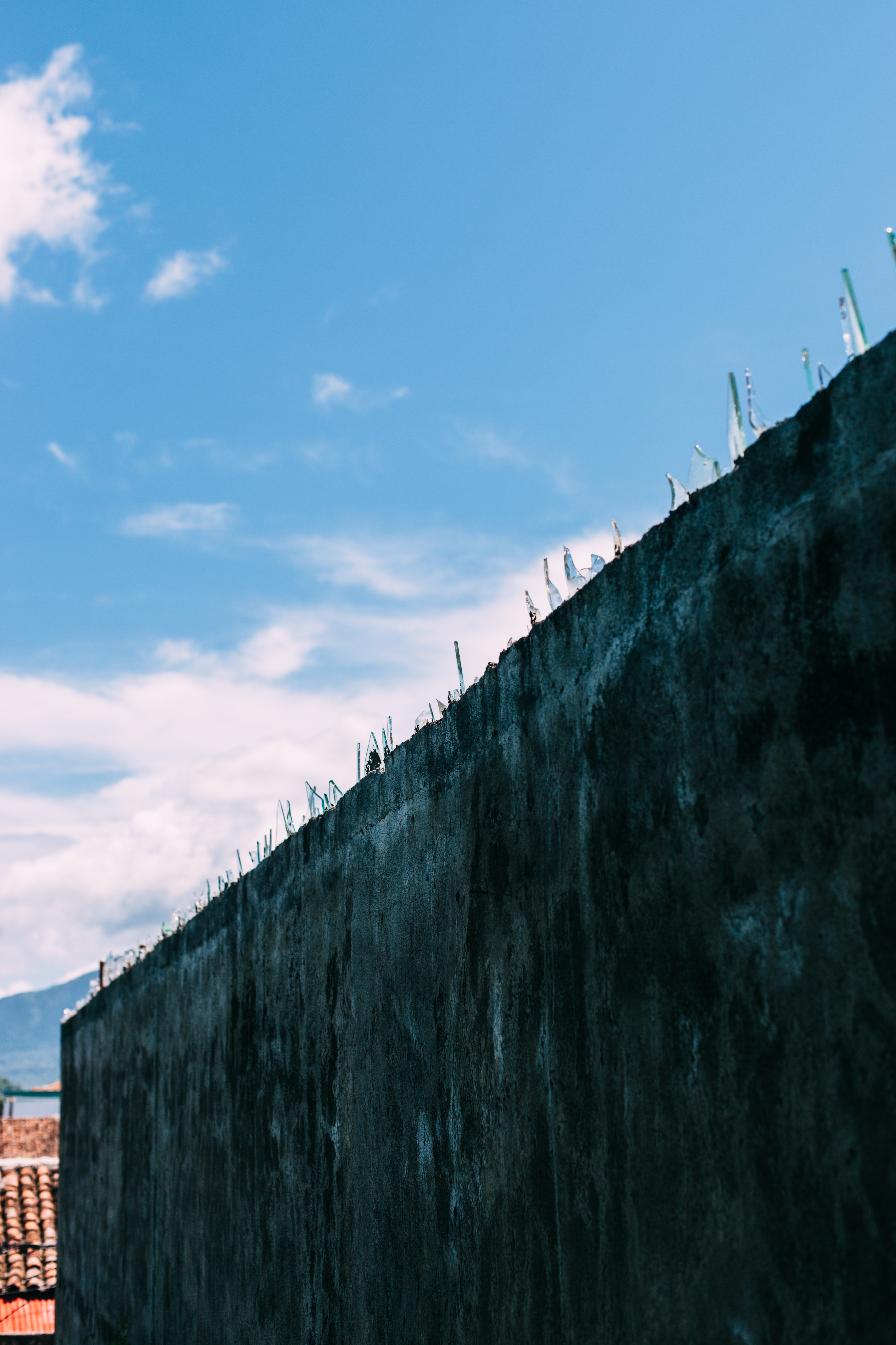 Weathered concrete wall topped with jagged broken glass shards against a blue sky in Nicaragua.