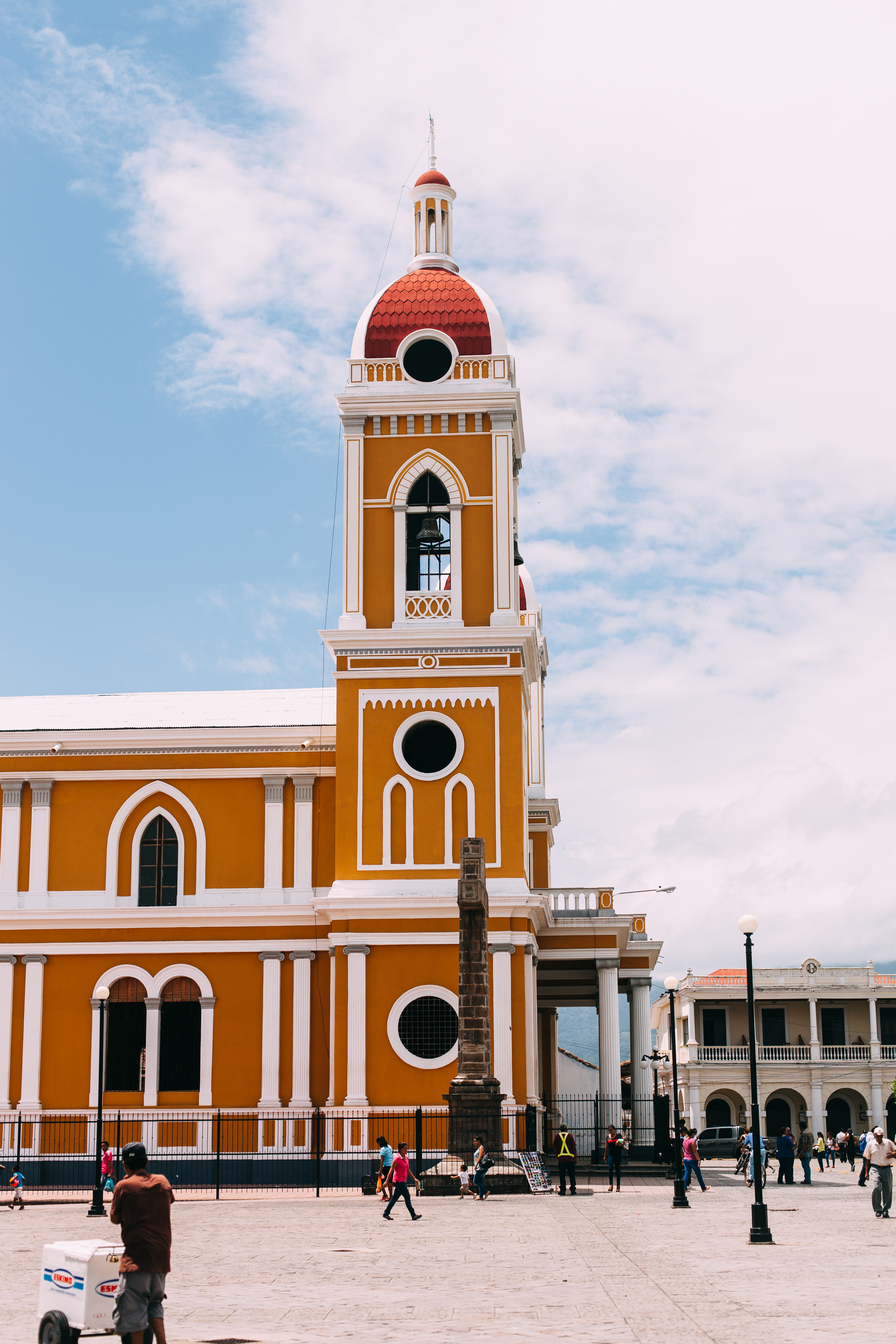 Yellow and white Granada Cathedral with red-domed bell tower rising above Parque Central in Nicaragua.