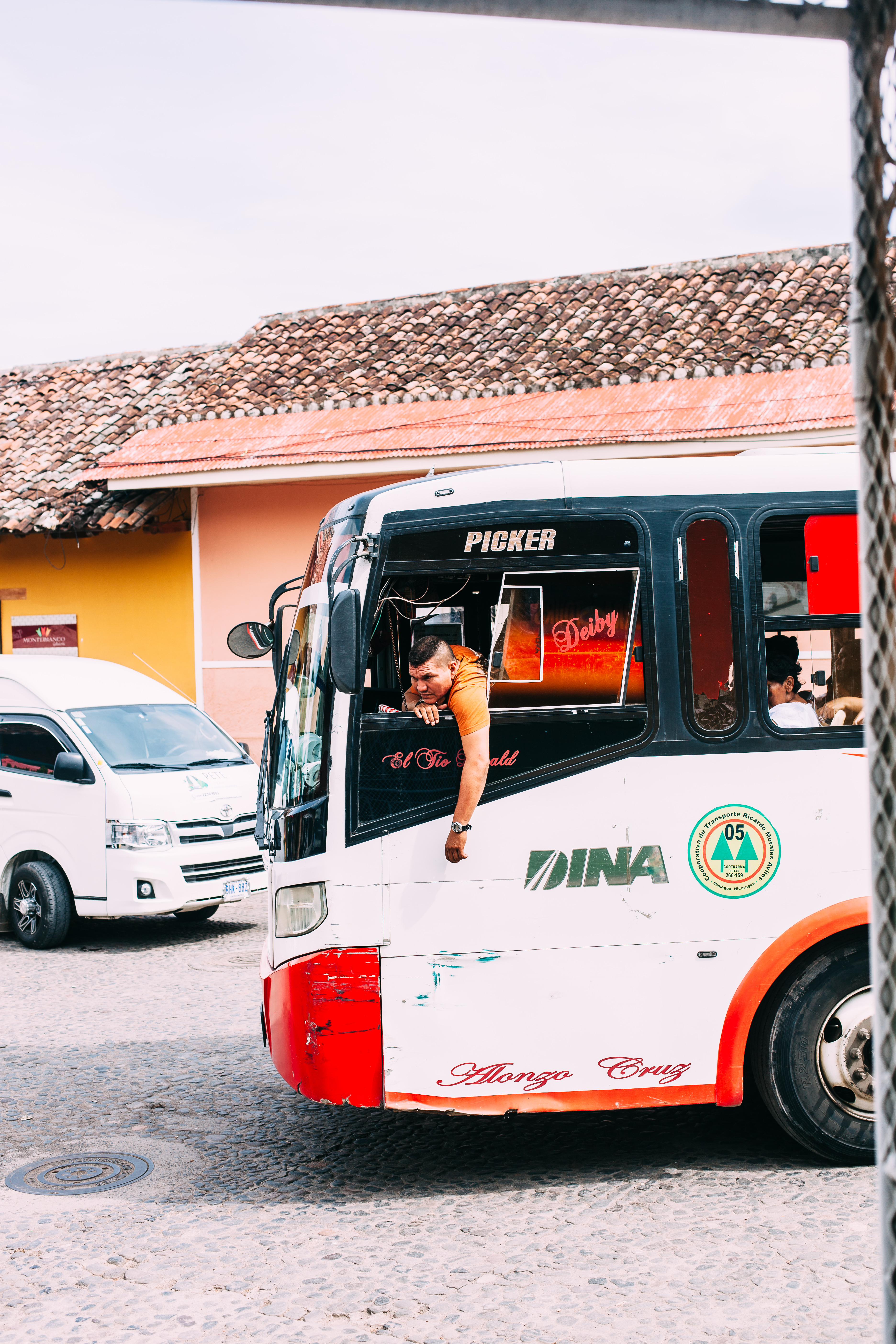 White and orange DINA commuter bus on a cobblestone street in Nicaragua with driver at the open window.