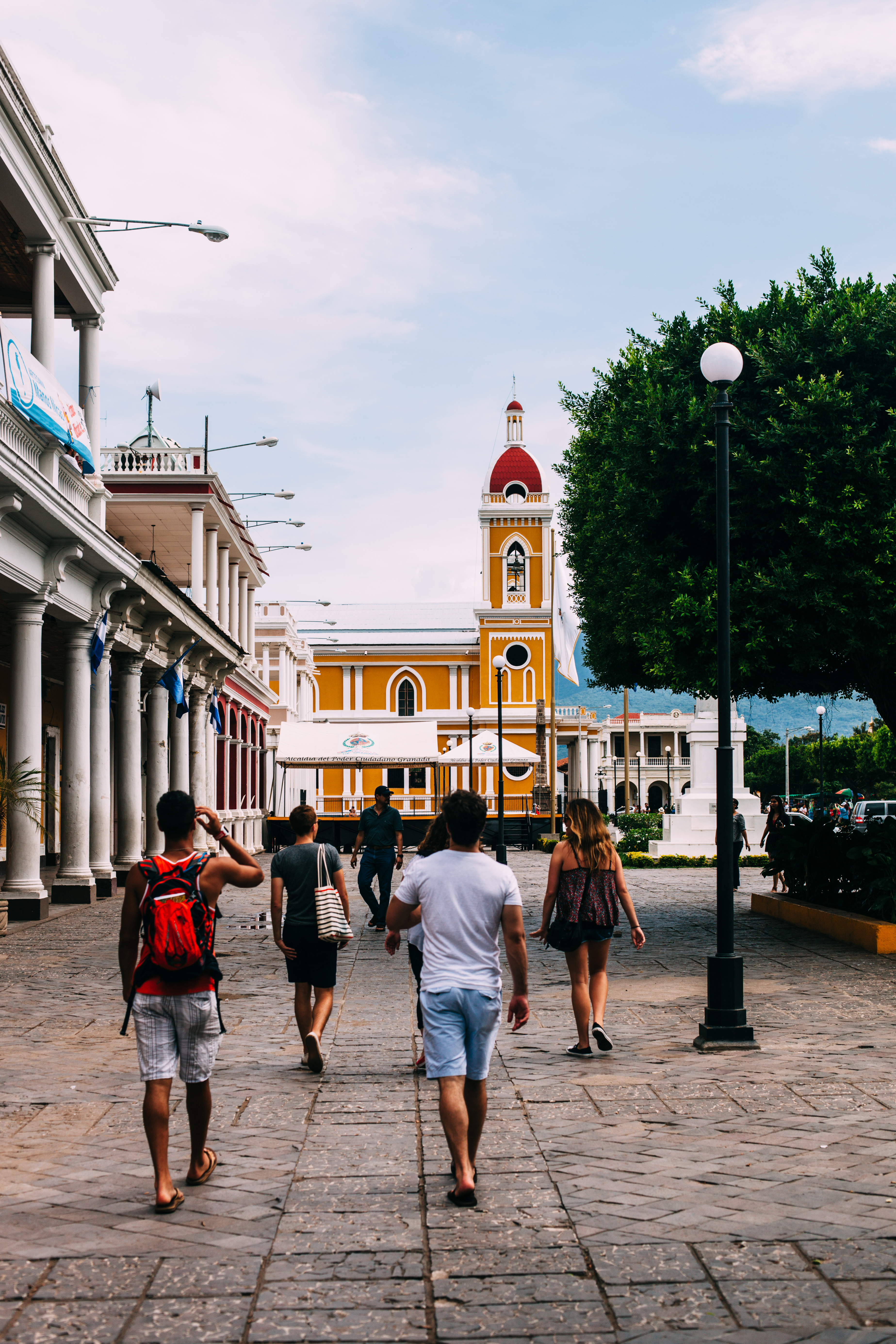 Friends walking across the stone plaza of Parque Central toward yellow Granada Cathedral in Nicaragua.