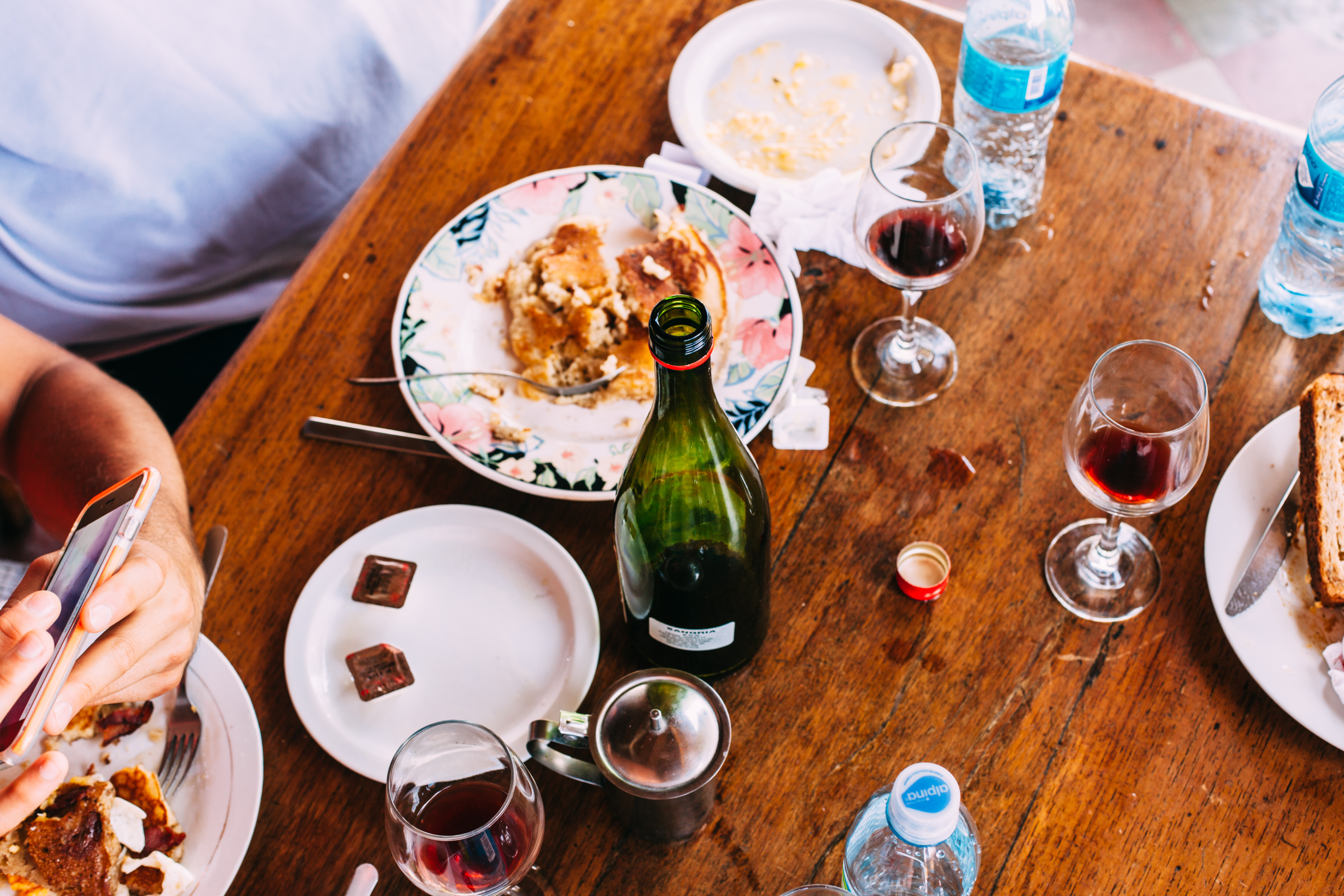 Overhead view of a wooden dining table after breakfast with pancake plates, wine glasses, and bottles.