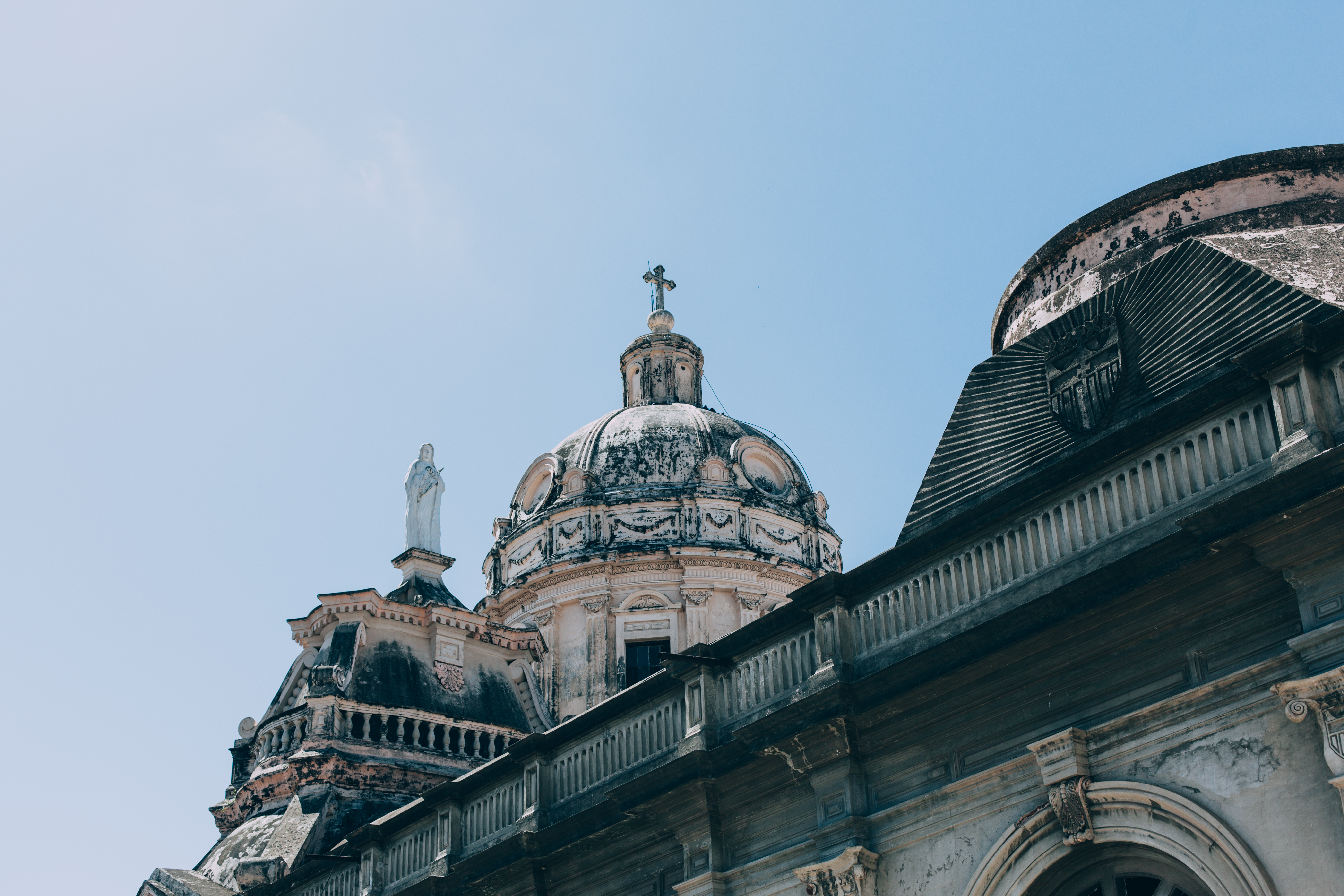 Weathered stone dome and statue of Iglesia de la Merced in Granada, Nicaragua against a blue sky.