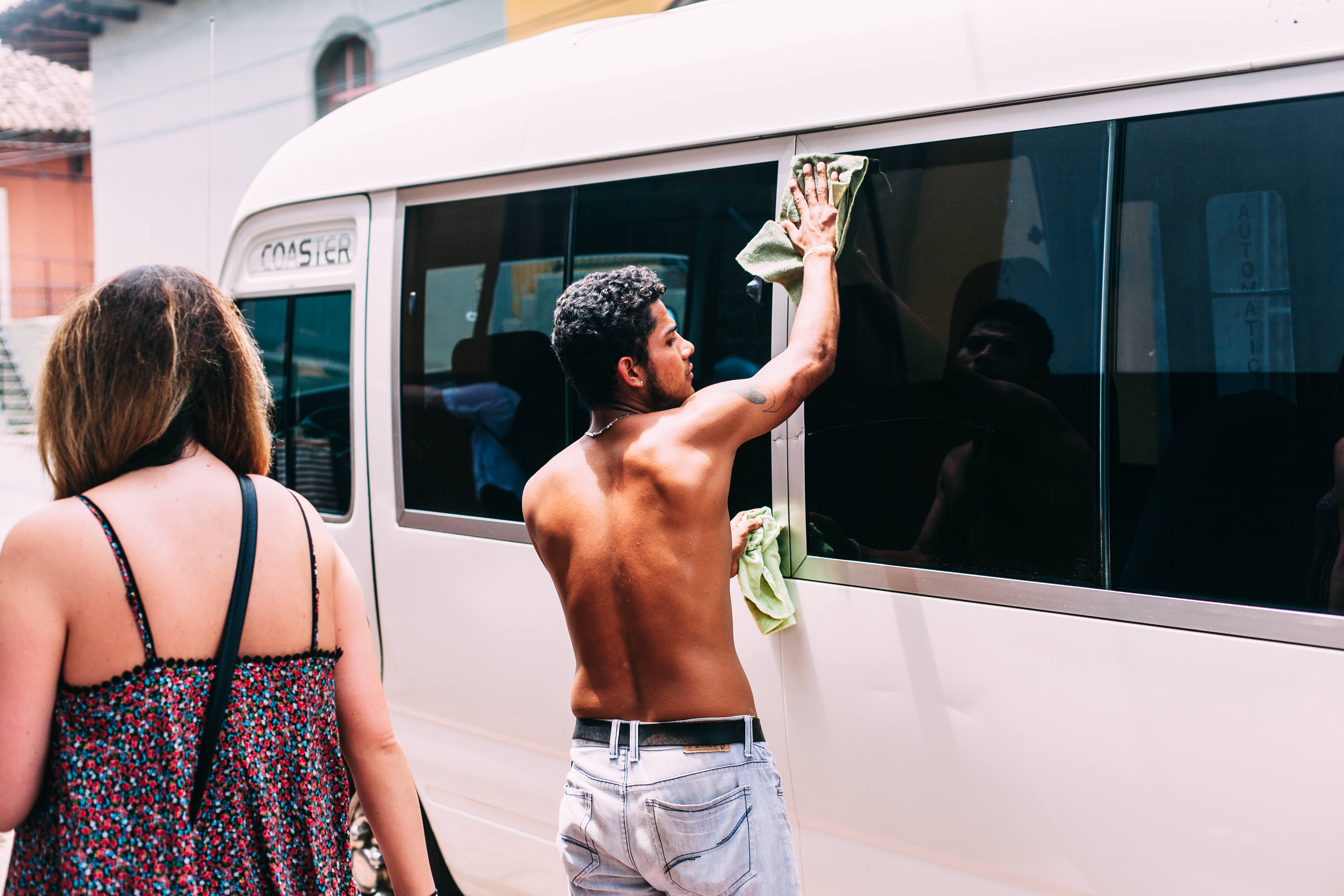 Shirtless man wiping down the side windows of a white Toyota passenger van in Granada, Nicaragua.
