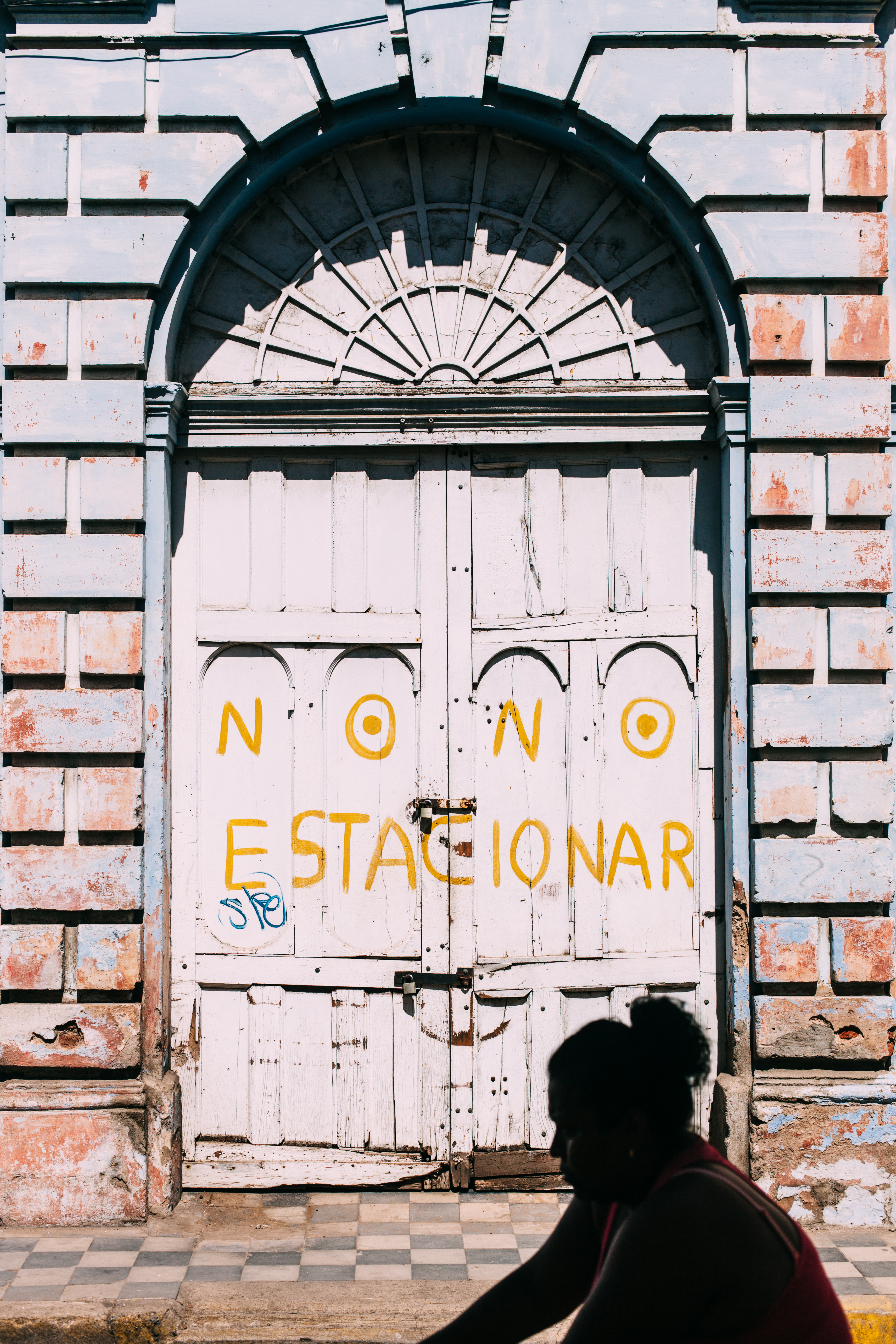 Bicyclist passing an arched white door with painted 'NO NO ESTACIONAR' lettering in Granada, Nicaragua.