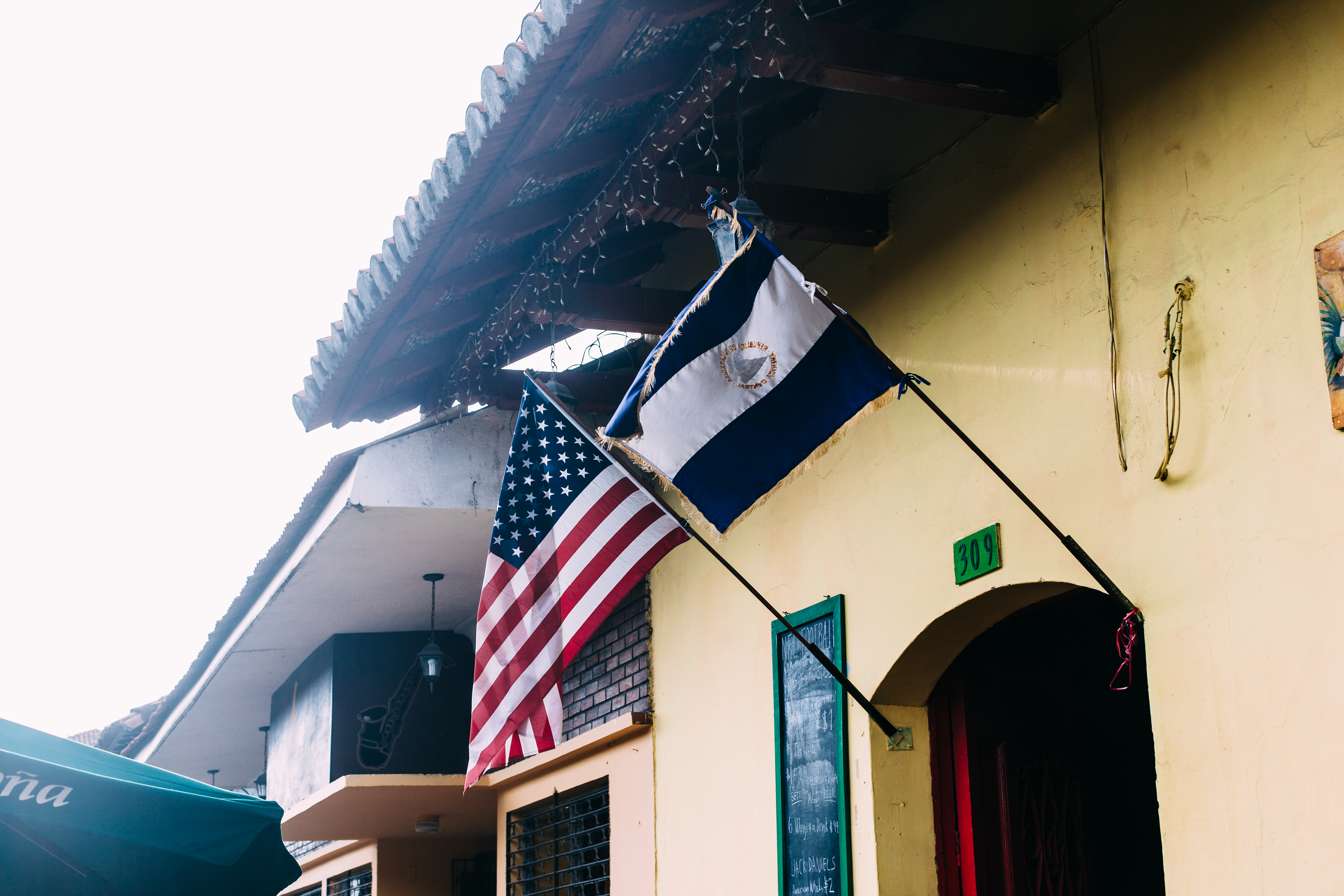 An American flag and a Nicaraguan flag hanging side-by-side above an arched doorway of a yellow colonial building with a chalkboard drink menu in Granada, Nicaragua, shot with a Canon 5D Mark II.