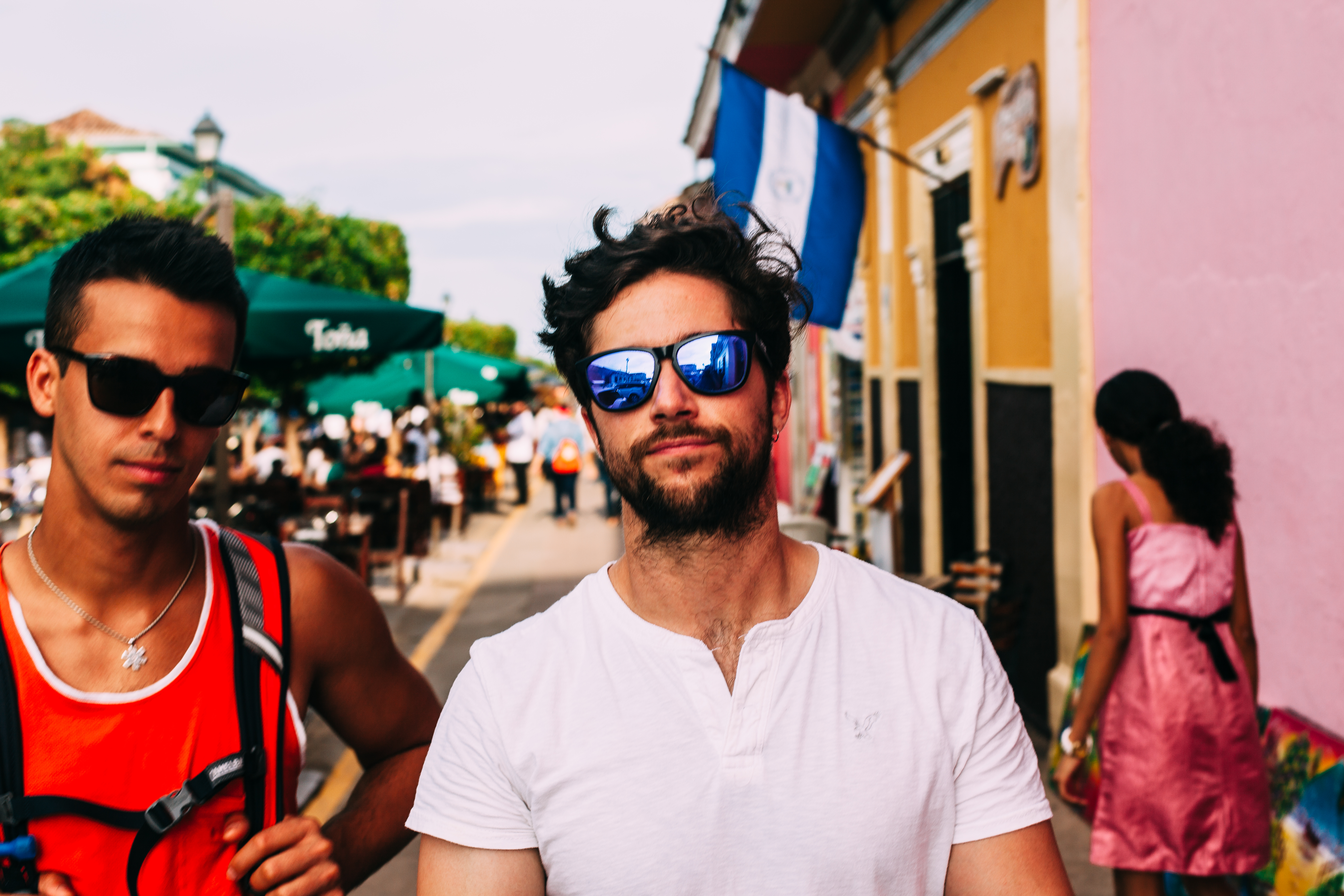 Portrait of two young men walking on a street in Granada, Nicaragua, with the man in front wearing a white henley and reflective sunglasses and his friend in an orange tank top beside him, shot with a Canon 5D Mark II.