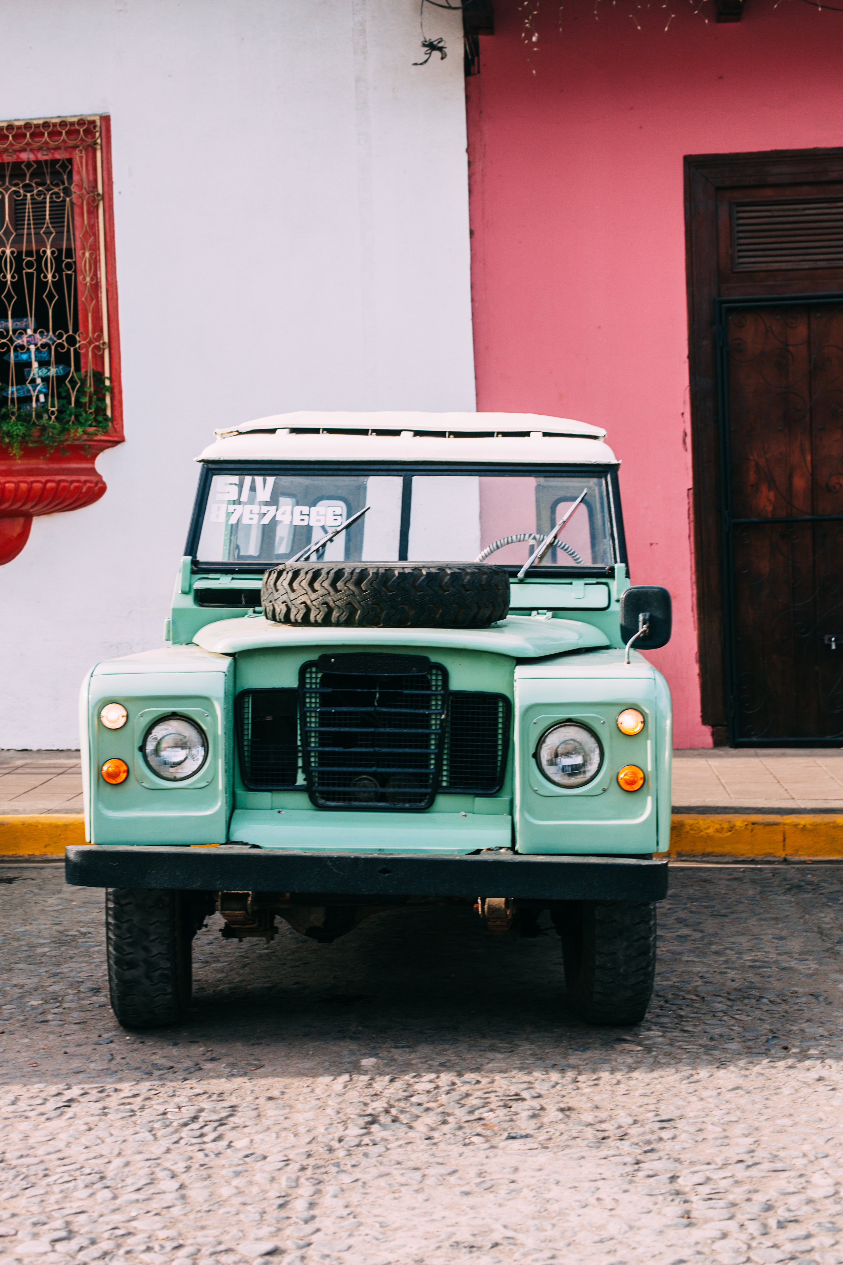 A vintage mint green Land Rover Series II with a spare tire mounted on the hood parked on a cobblestone street in Granada, Nicaragua, shot with a Canon 5D Mark II.