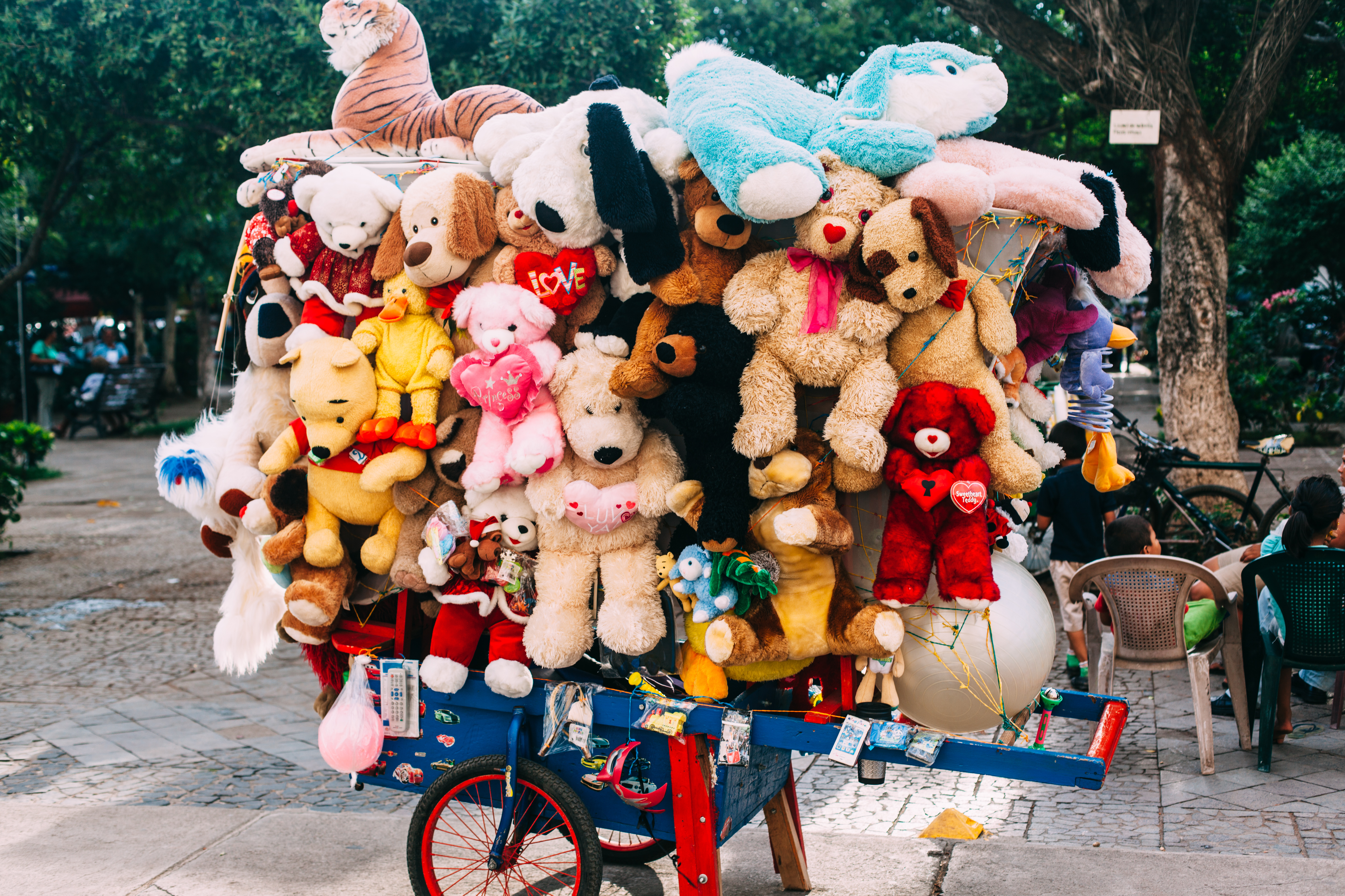 Colorful vendor cart overflowing with plush teddy bears in a town plaza park in Granada, Nicaragua.
