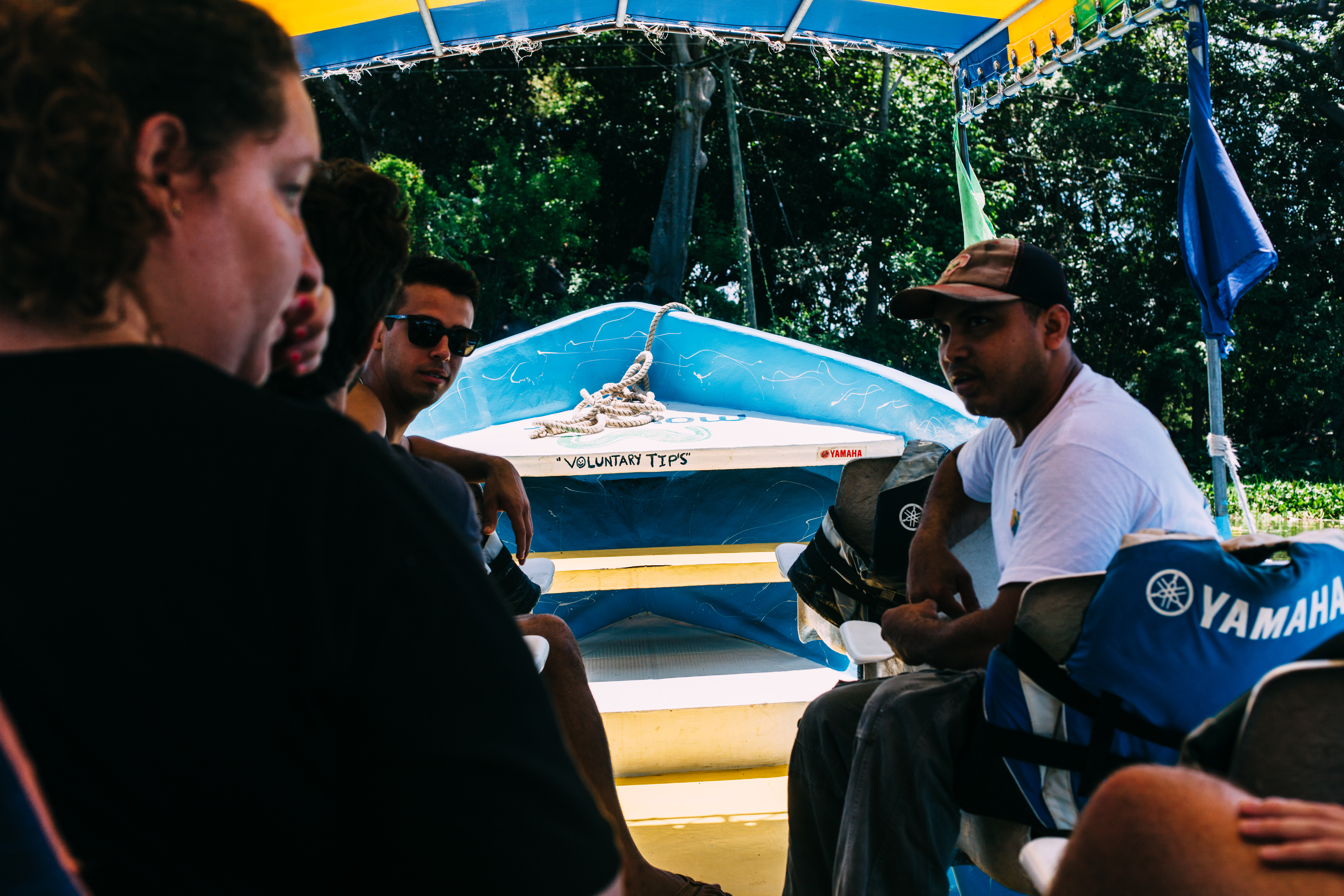 Passengers in a canopy boat on Lake Nicaragua with captain and a handwritten 'VOLUNTARY TIPS' sign.
