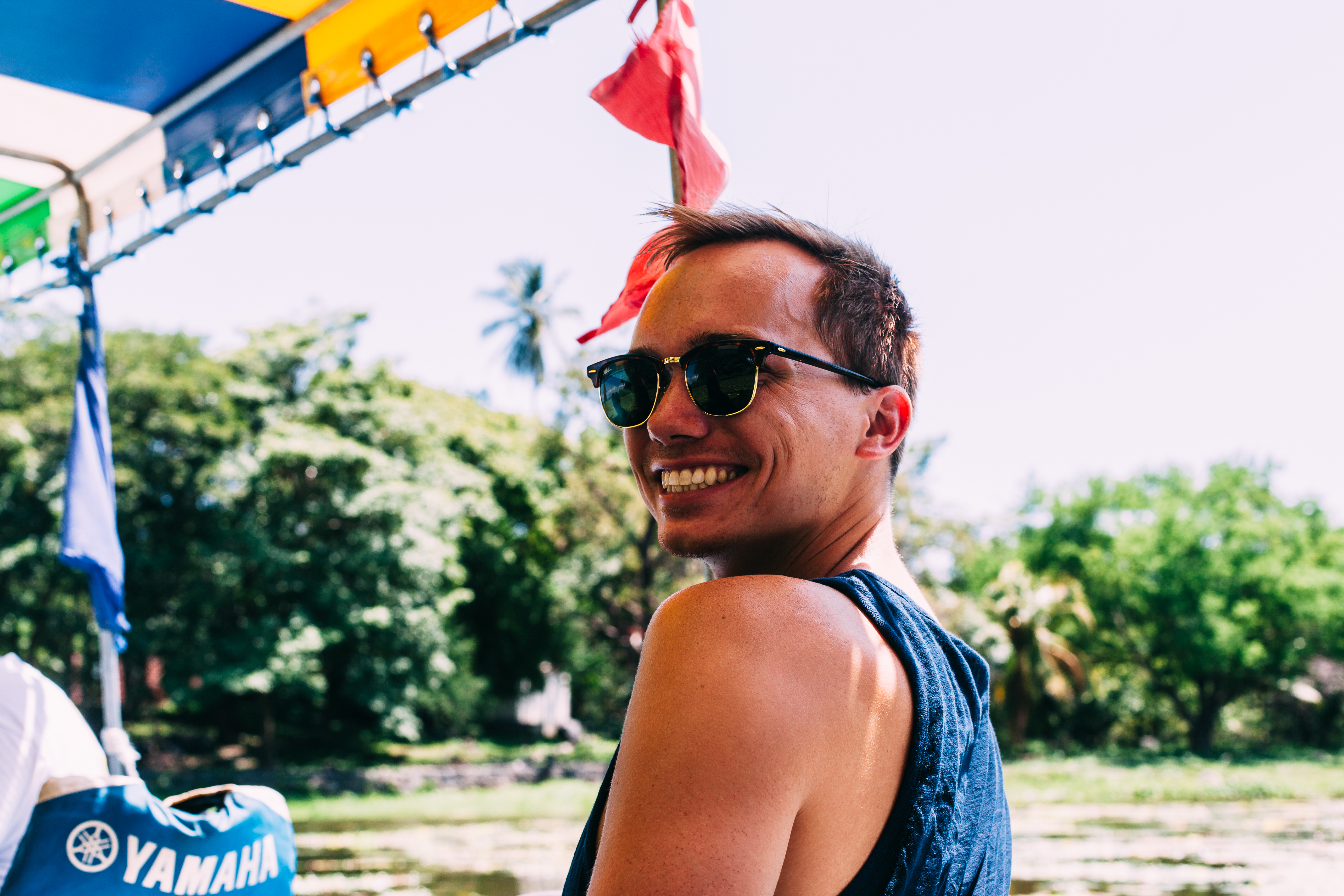 Grinning young man in sunglasses looking back over his shoulder during a boat ride under canopy awnings.