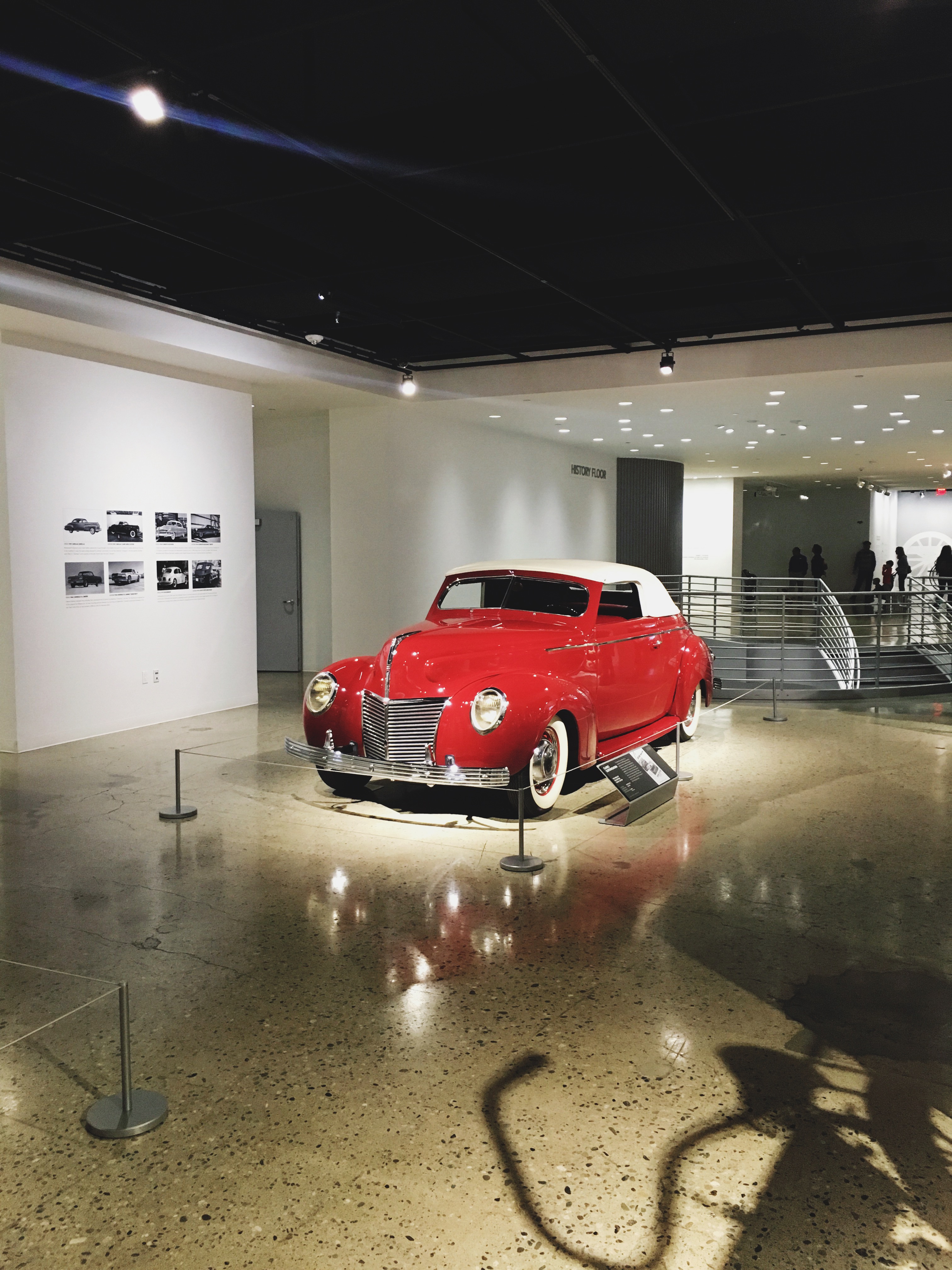 Glossy red vintage convertible coupe with white top and whitewall tires on a polished museum floor.