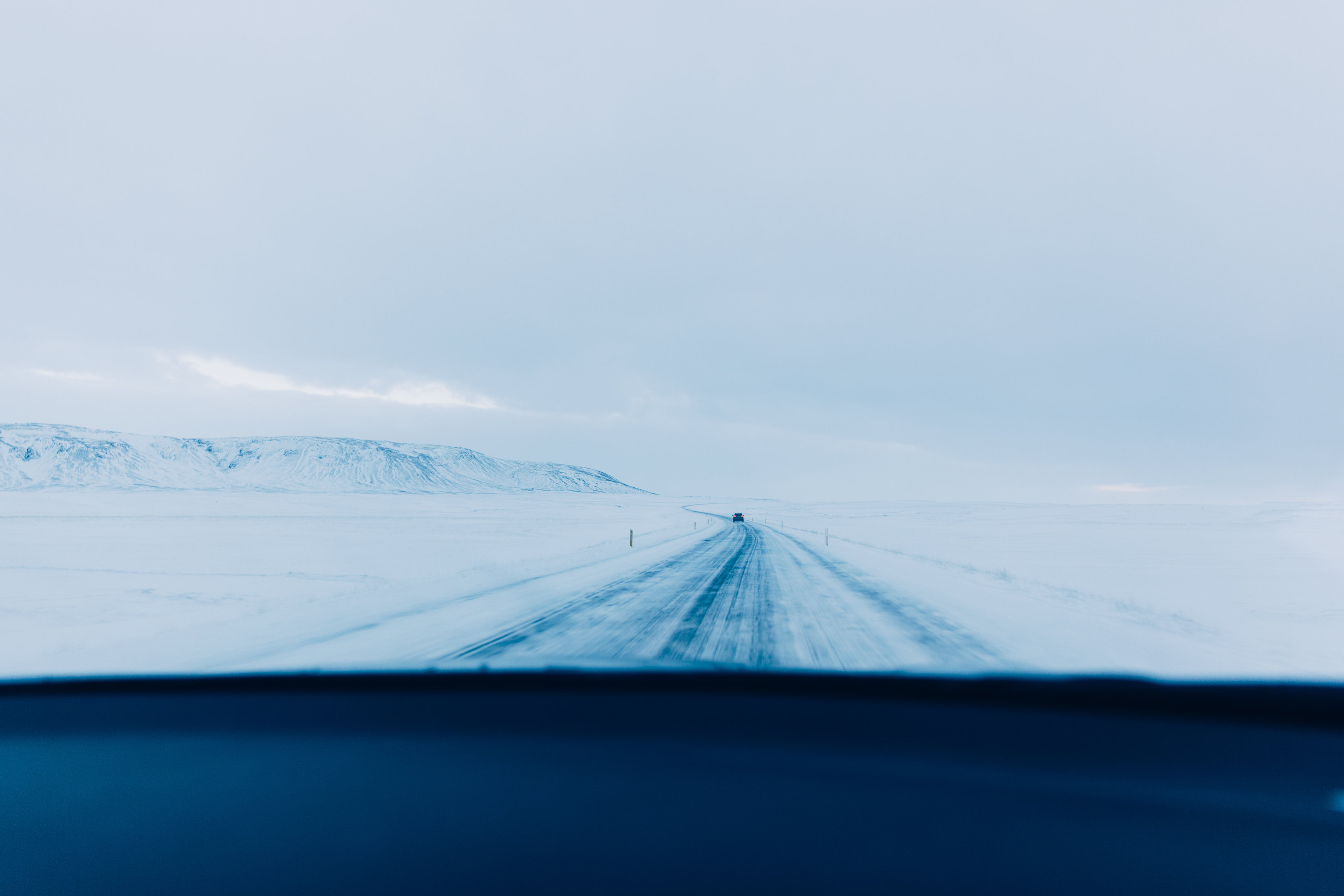 View from inside a vehicle driving down an icy, snow-covered highway across a desolate winter landscape in Iceland.