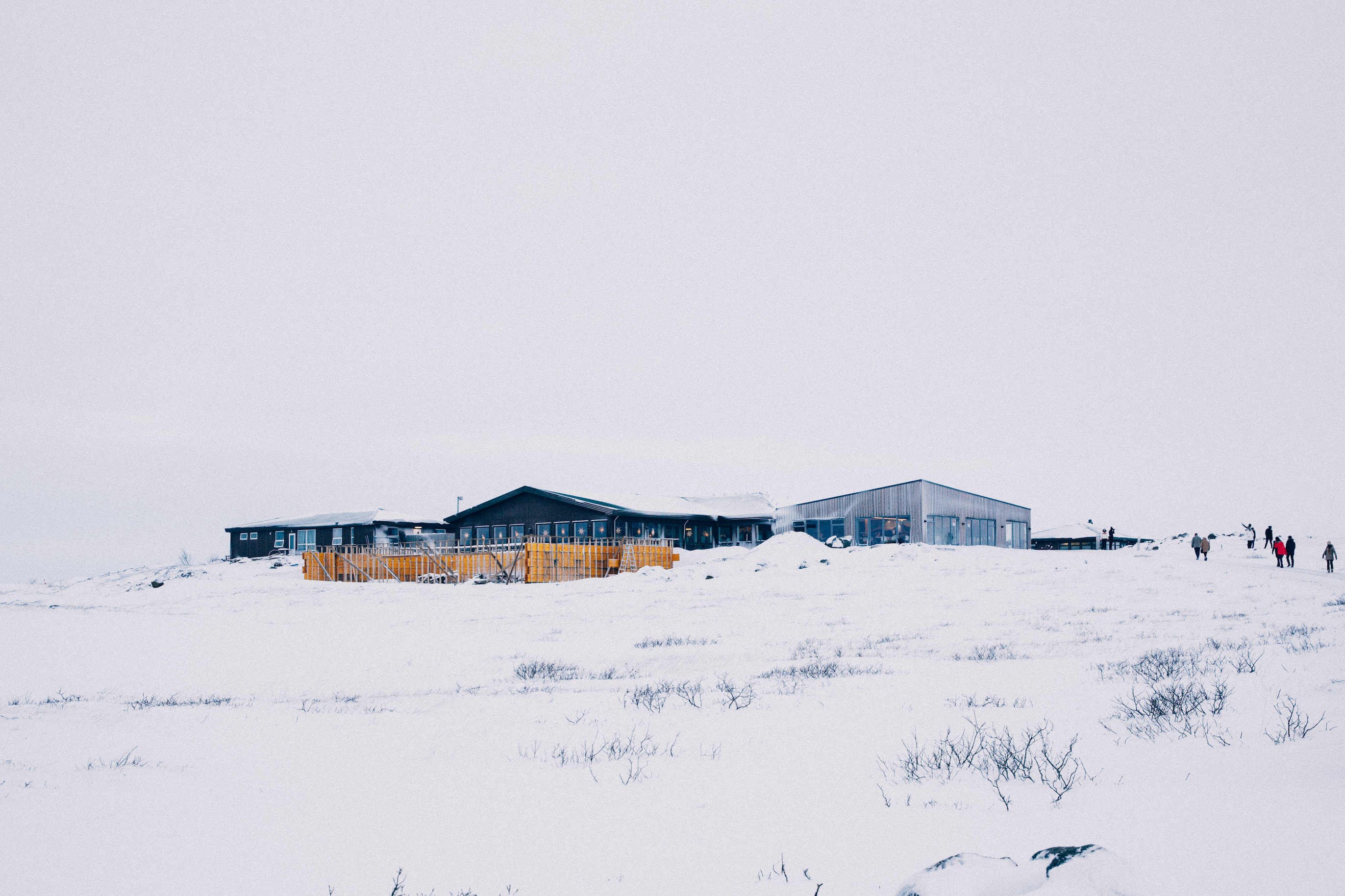 Modern visitor lodges and cabins on a snow-covered hill with people walking across terrain in Iceland.