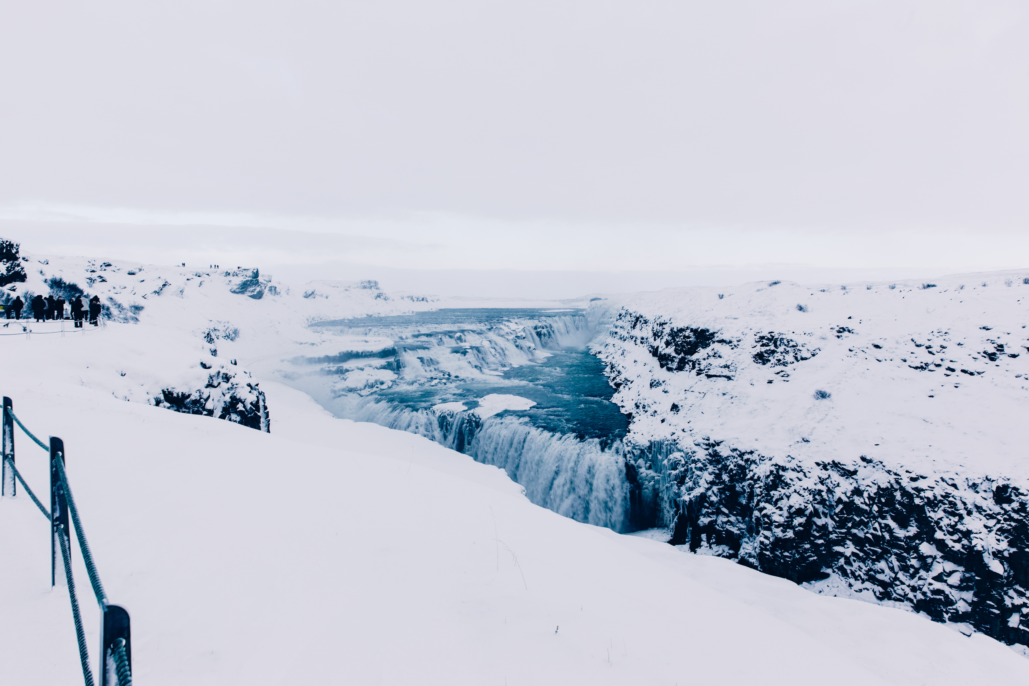 Dramatic tiered cascades of Gullfoss waterfall plunging into a frozen canyon flanked by ice in Iceland.