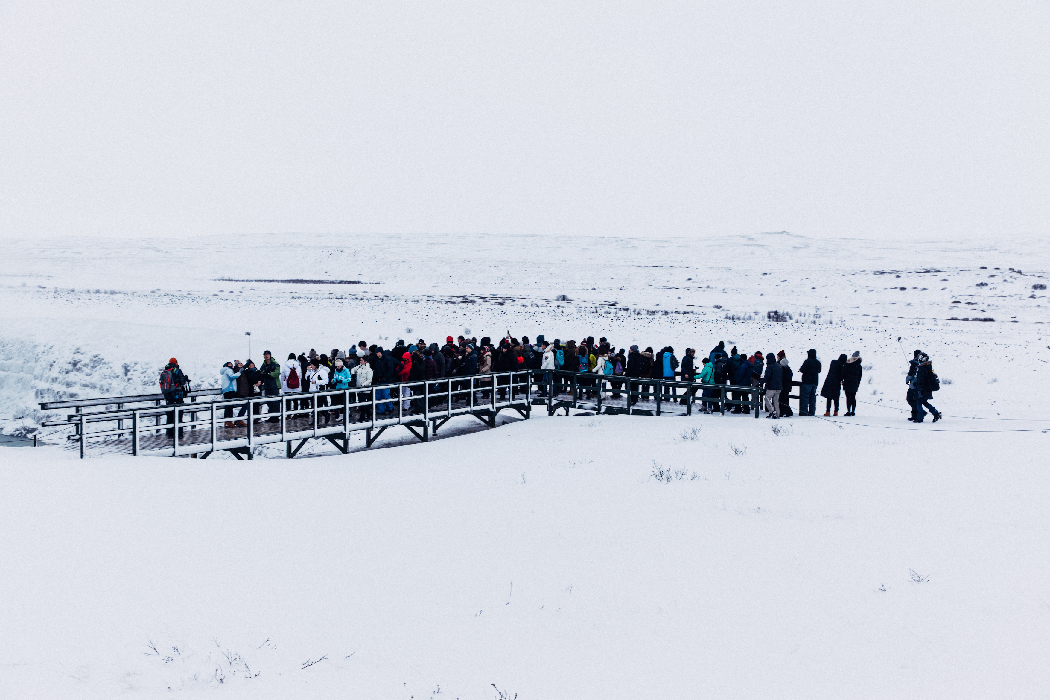 Tourists standing along an elevated wooden observation walkway overlooking snowy landscape in Iceland.