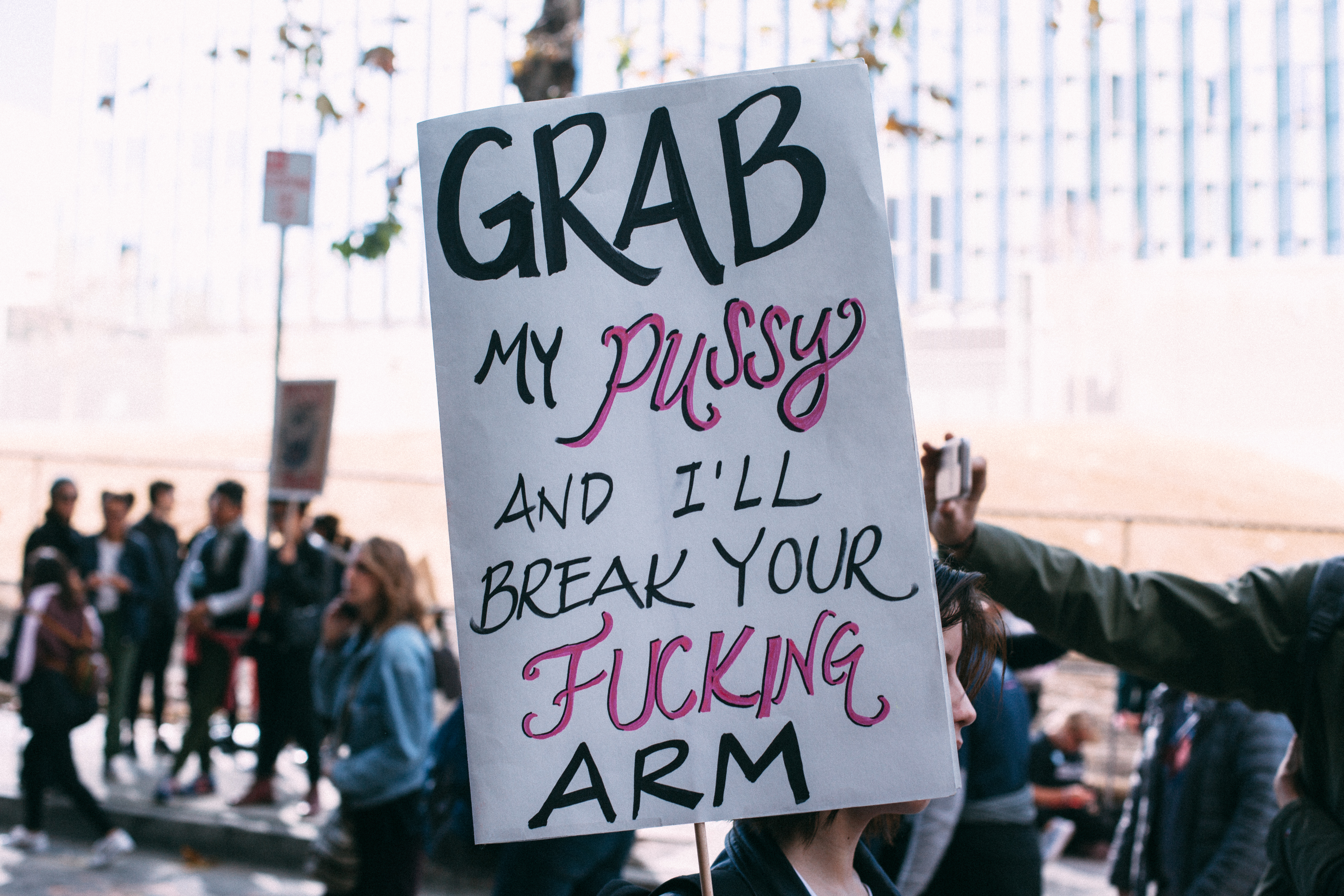 A protester holding up a handwritten poster sign reading 'Grab my pussy and I'll break your fucking arm' during the Women's March in Los Angeles, shot with a Canon 5D Mark II.