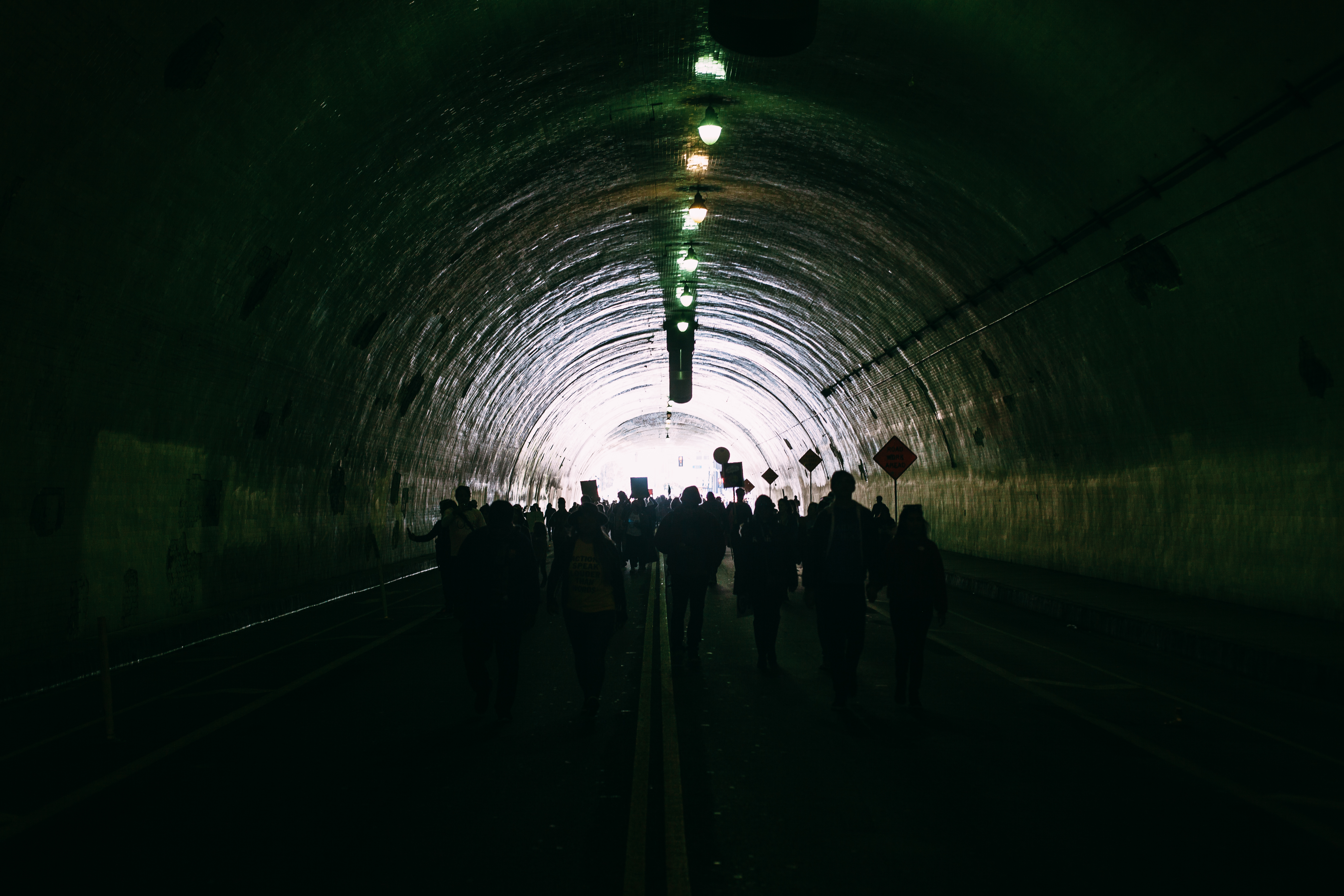 Crowds of protesters walking through the dark curving interior of the 2nd Street Tunnel toward the daylight at the exit during the Women's March in Los Angeles, shot with a Canon 5D Mark II.