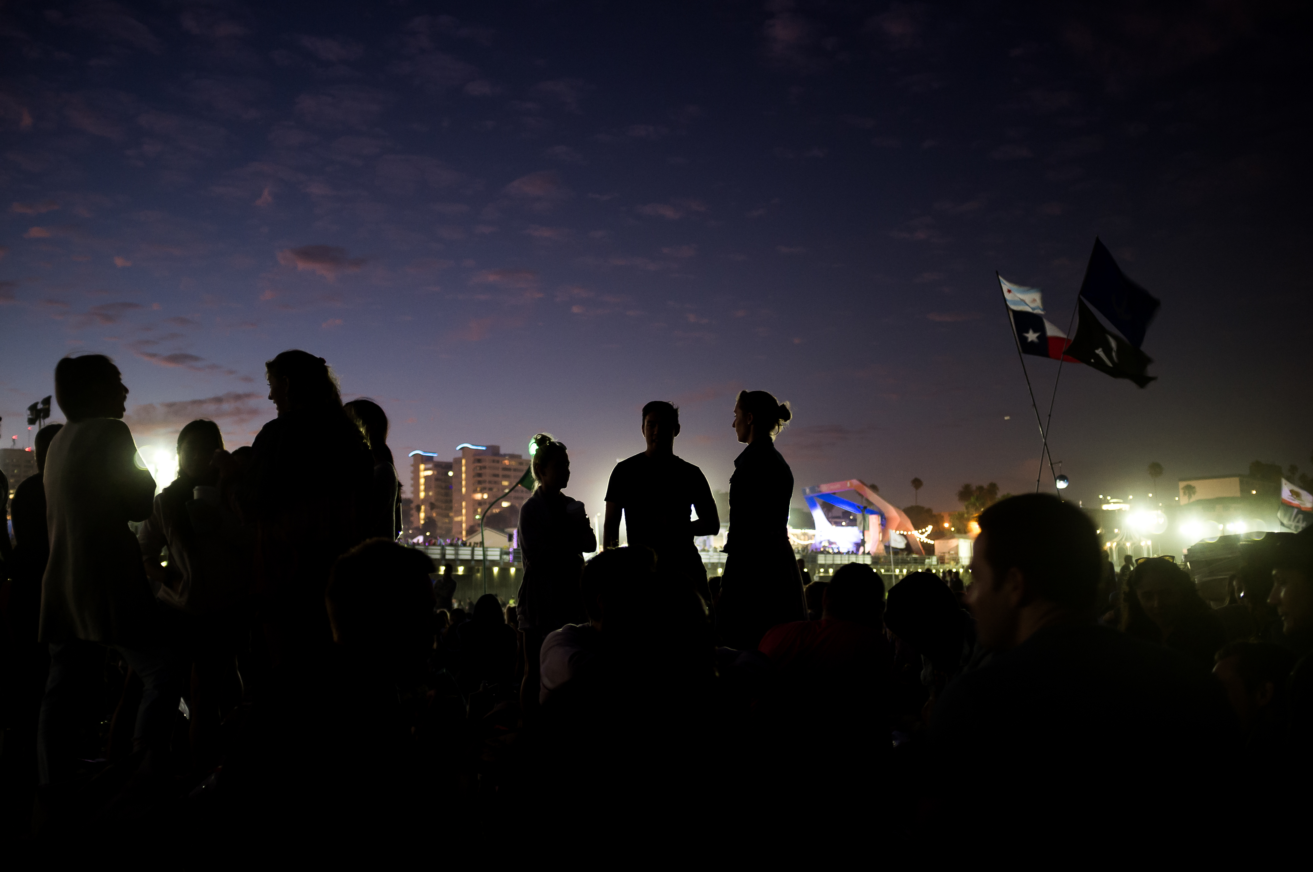 Concertgoers gathered on the beach at twilight with city lights during the Santa Monica Pier concert.