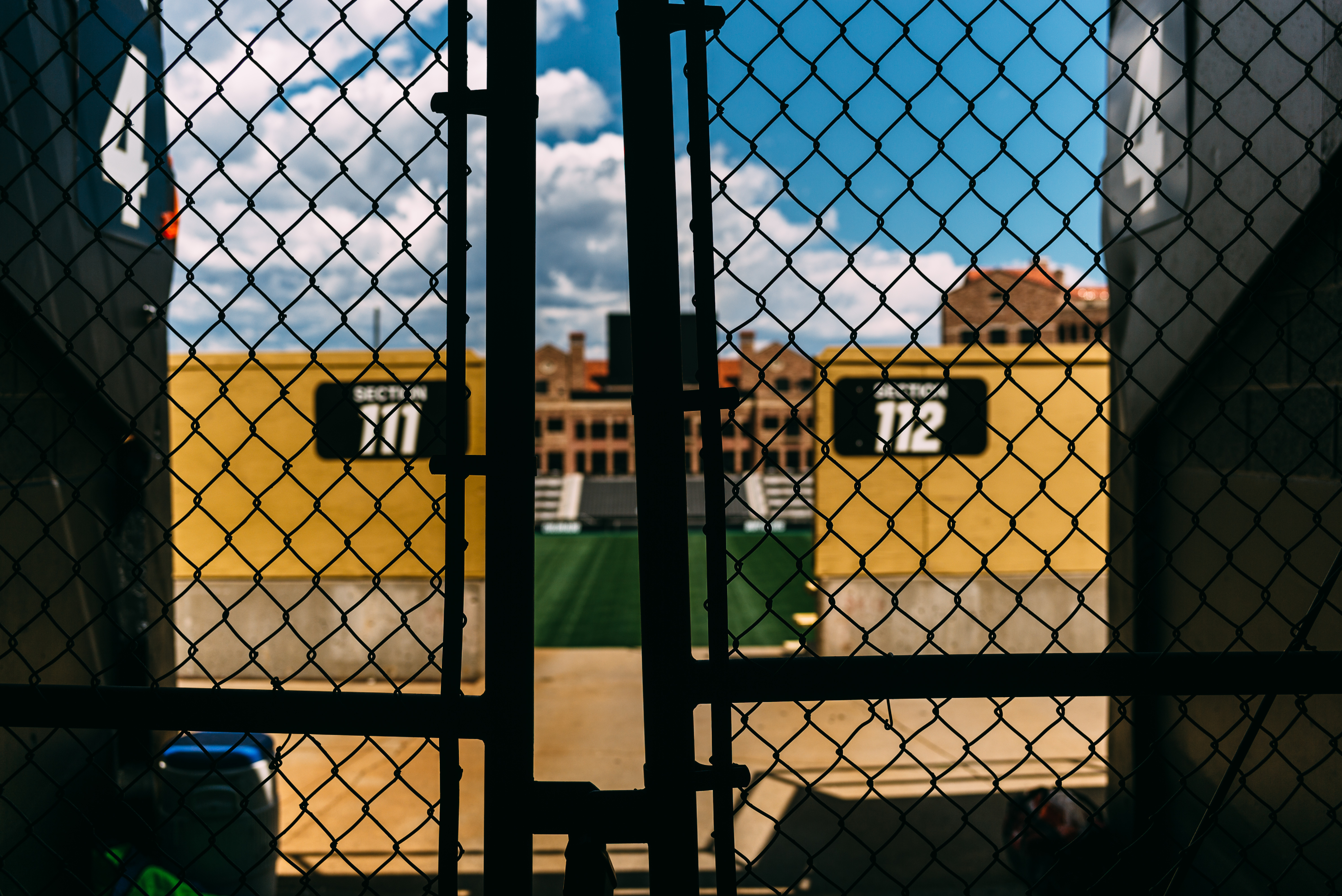 Looking through a chain-link gate toward a football stadium with yellow walls marked Section 111 and 112.