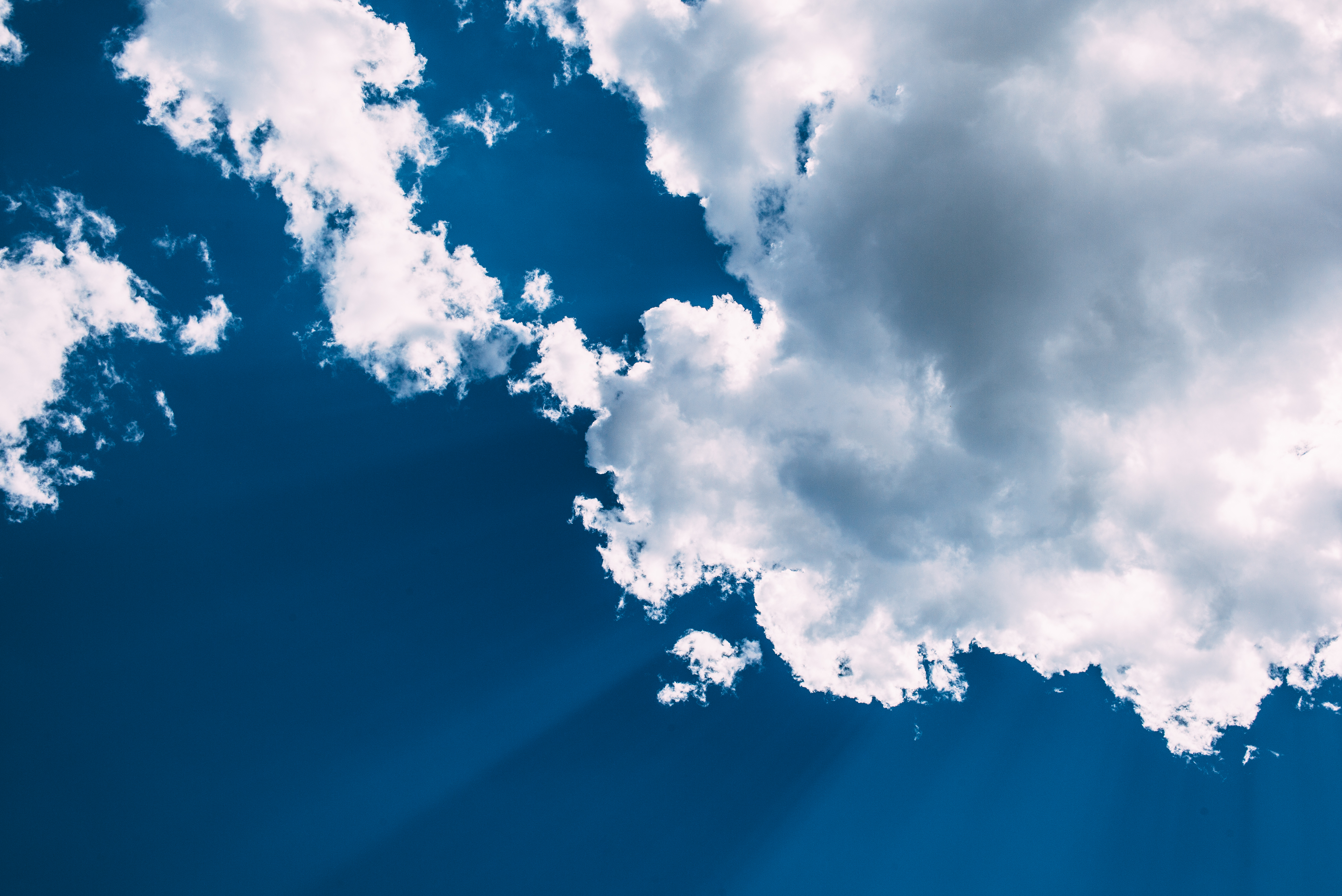 Fluffy white cumulus clouds set against a deep blue sky with subtle sun rays streaming downward.