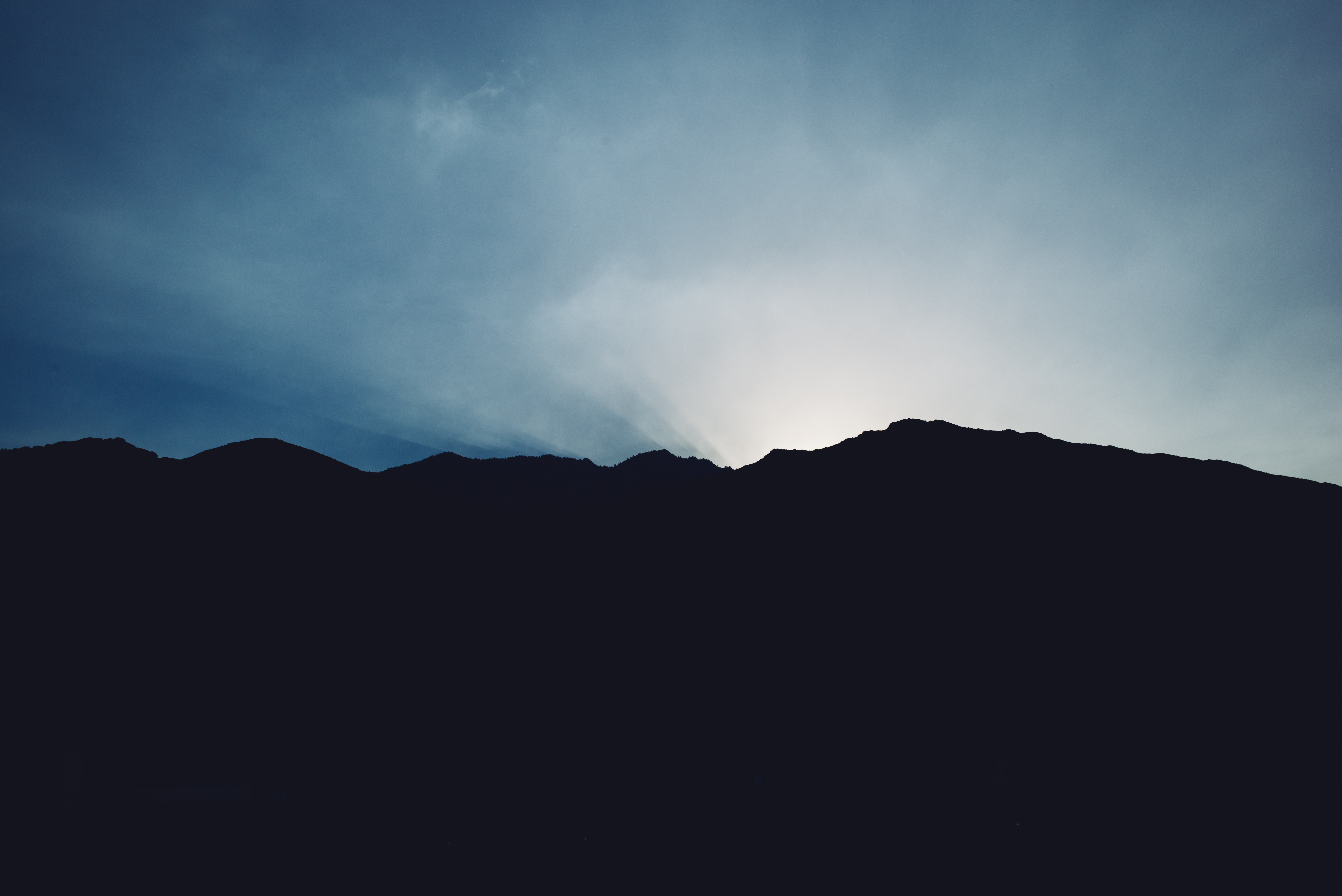 Rugged mountain ridge silhouetted by bright crepuscular rays in a deep blue evening sky in Palm Springs.