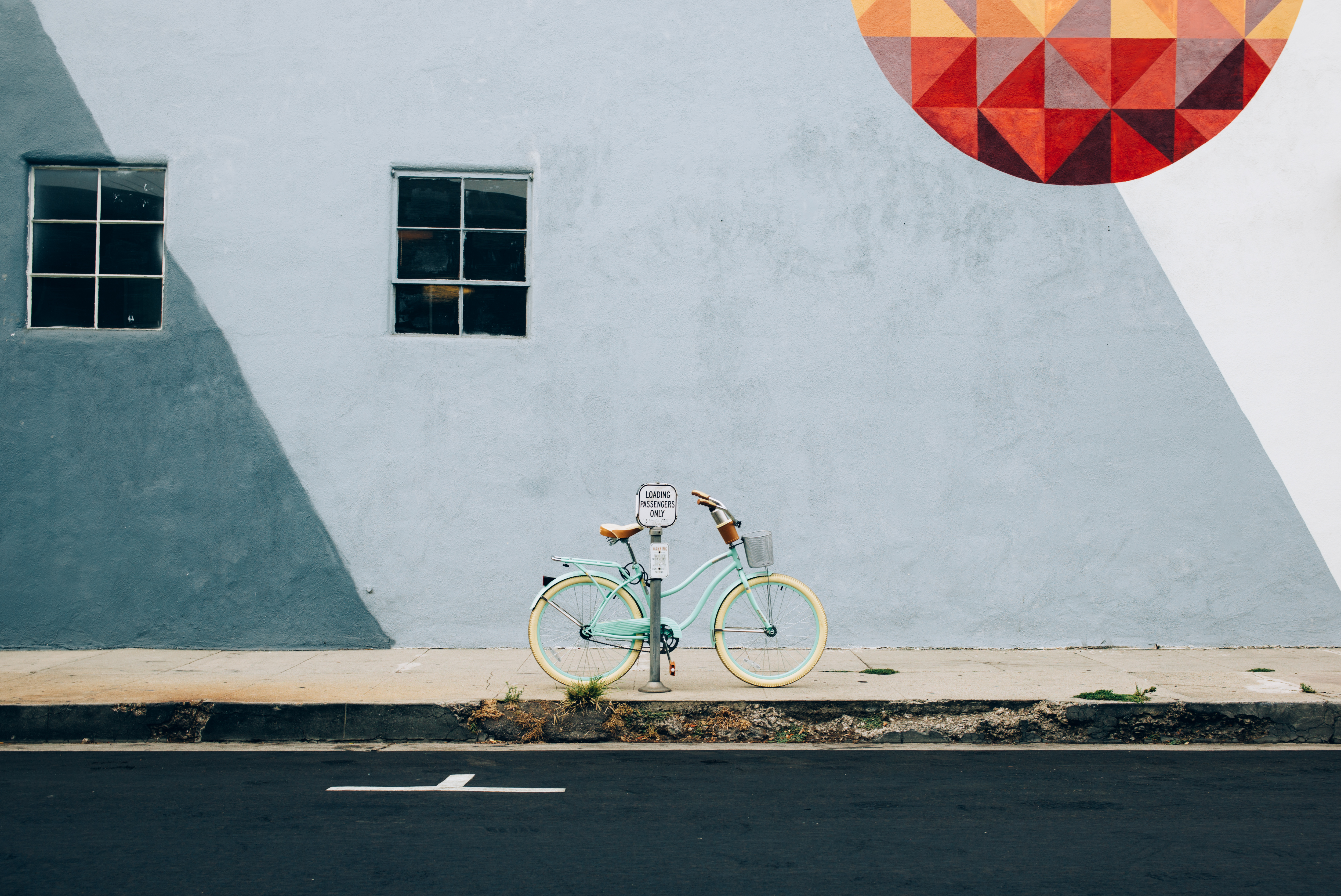Mint green cruiser bike parked on a sidewalk in front of a pastel geometric mural with a red circle.