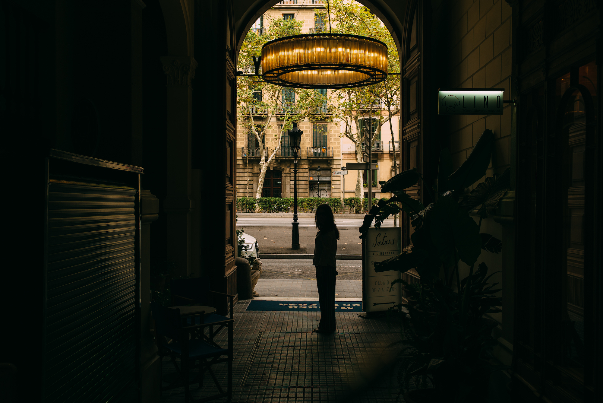 Person silhouetted beneath a circular chandelier in an arched entrance overlooking a Barcelona street.