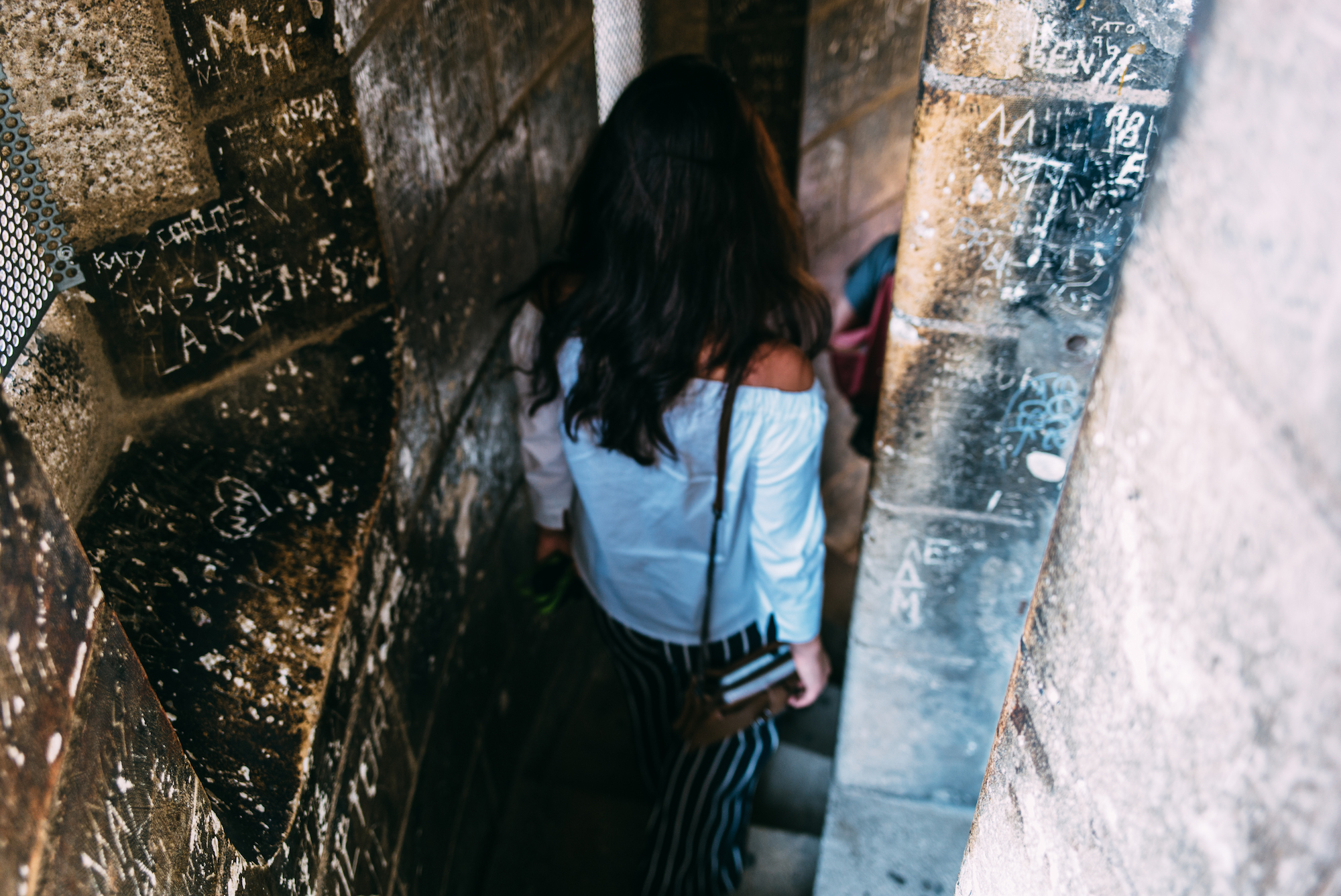 Woman walking down a historic stone spiral staircase with walls covered in carved graffiti in Barcelona.