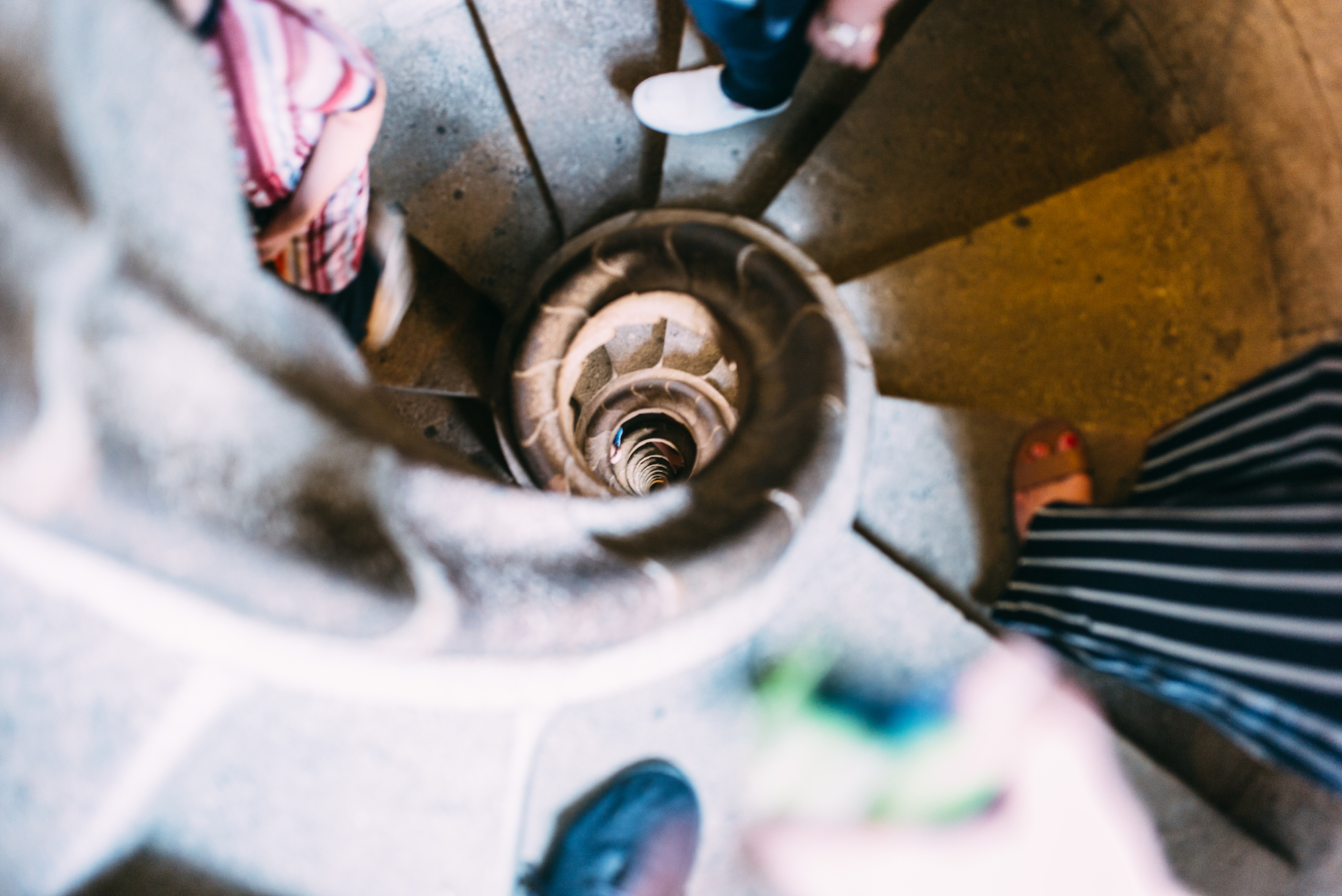 Looking down the center of a dizzying stone spiral staircase as visitors descend a historic Barcelona tower.