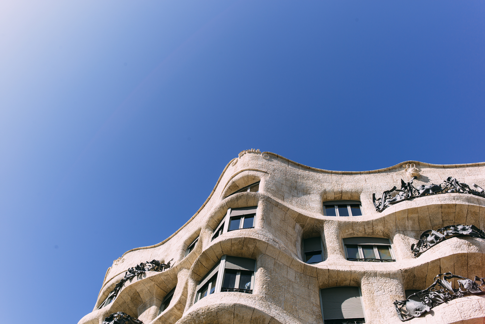 Undulating stone facade and wrought-iron balconies of Antoni Gaudí's Casa Milà under a blue Barcelona sky.